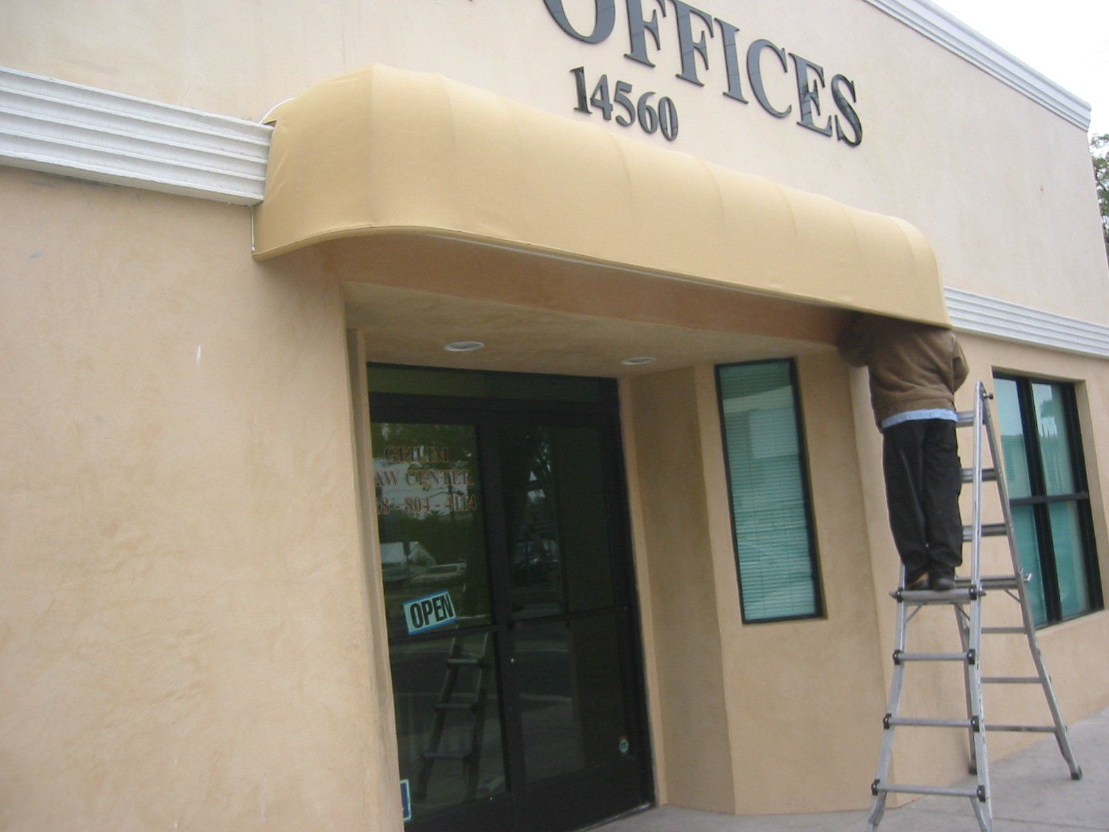 Person on ladder painting exterior of beige office building above glass entrance.