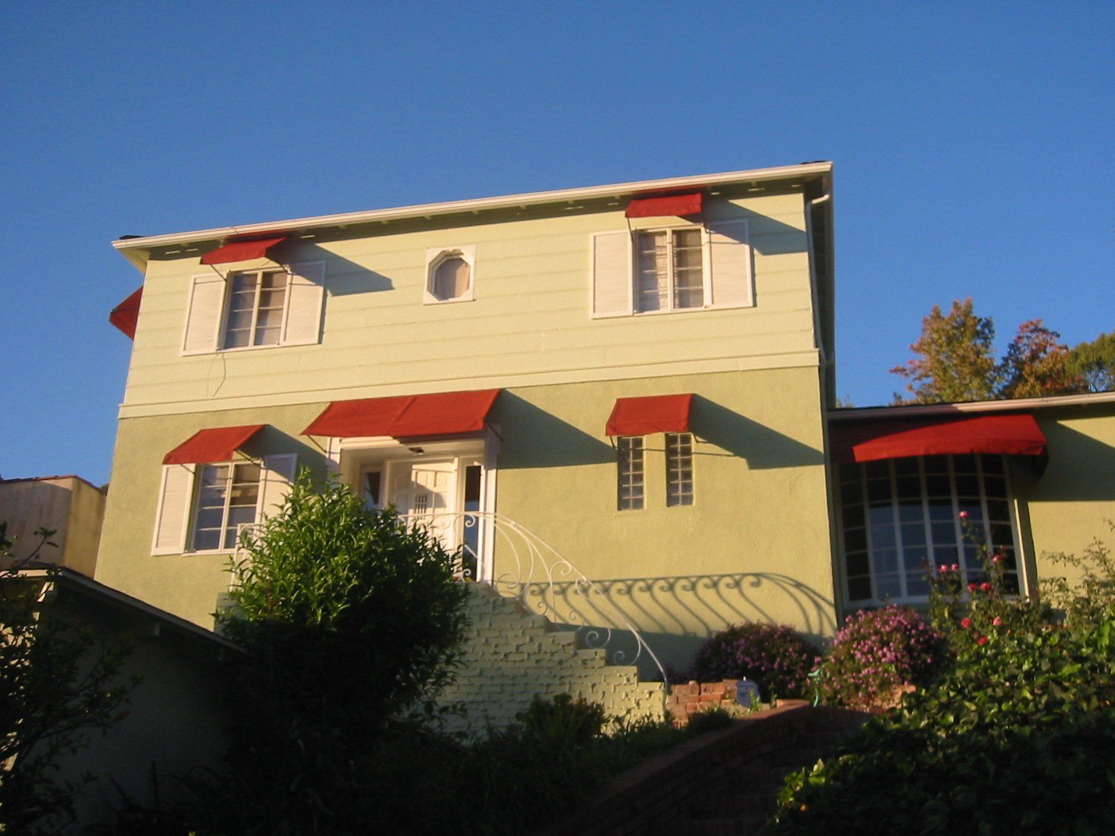 Two-story yellow house with red awnings on a sunny hillside