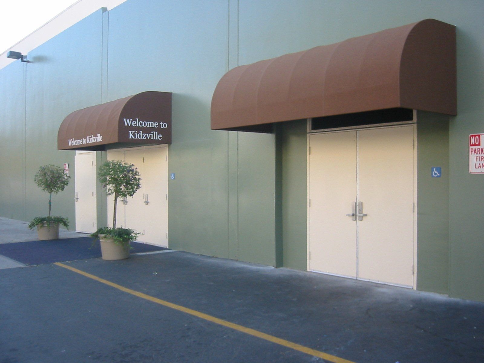Exterior of a building with brown awnings, double doors, and a parking lot walkway nearby