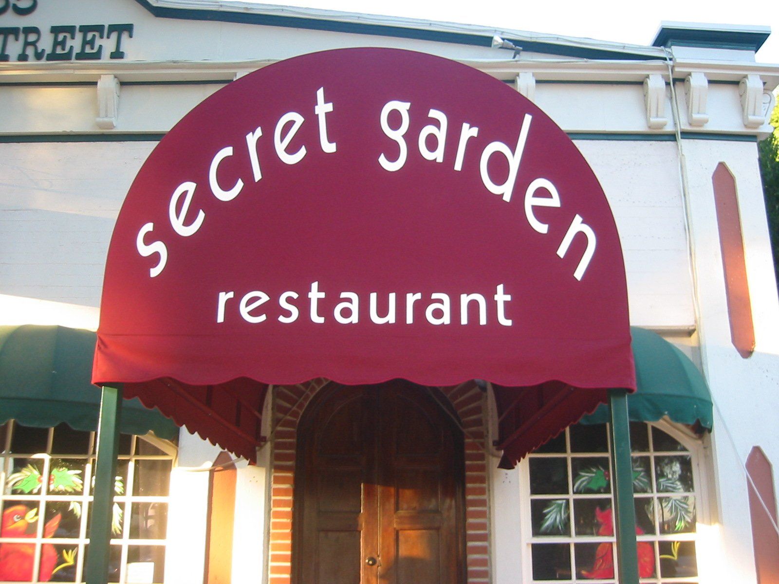Red awning reading “secret garden restaurant” over a wooden entrance