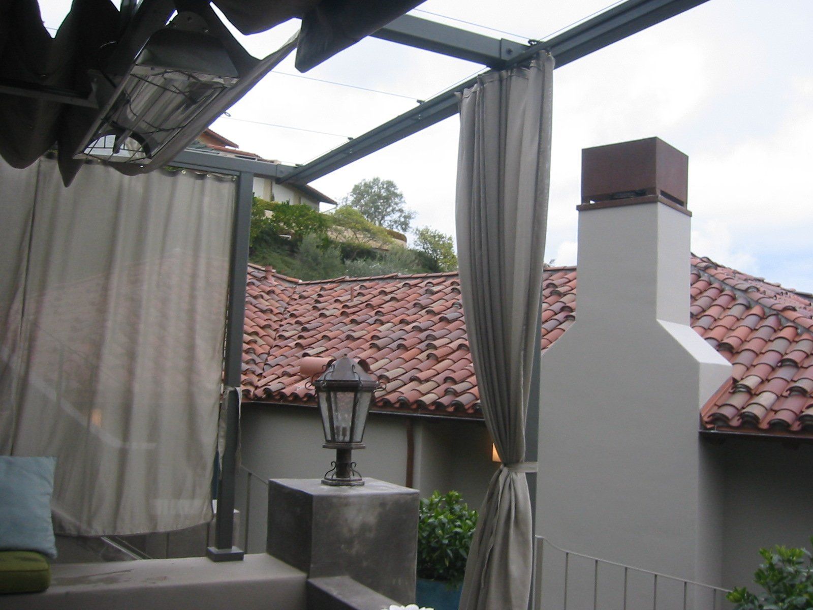 Patio with gray curtains, a lantern on a table, and red-tiled roof under a pergola