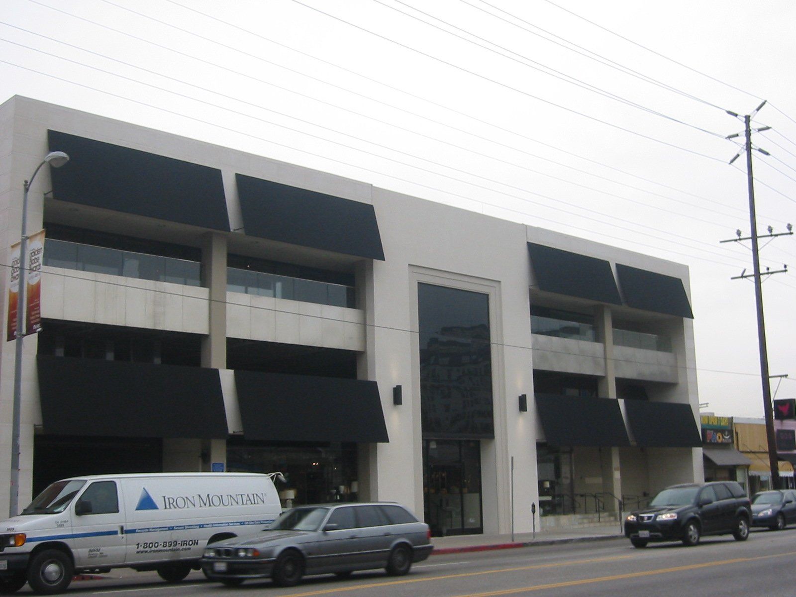 Street view of a modern office building with parked vans and cars on a cloudy day
