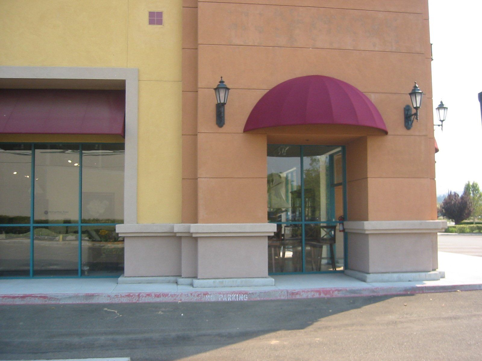Storefront entrance with maroon awning and glass doors in a beige shopping center