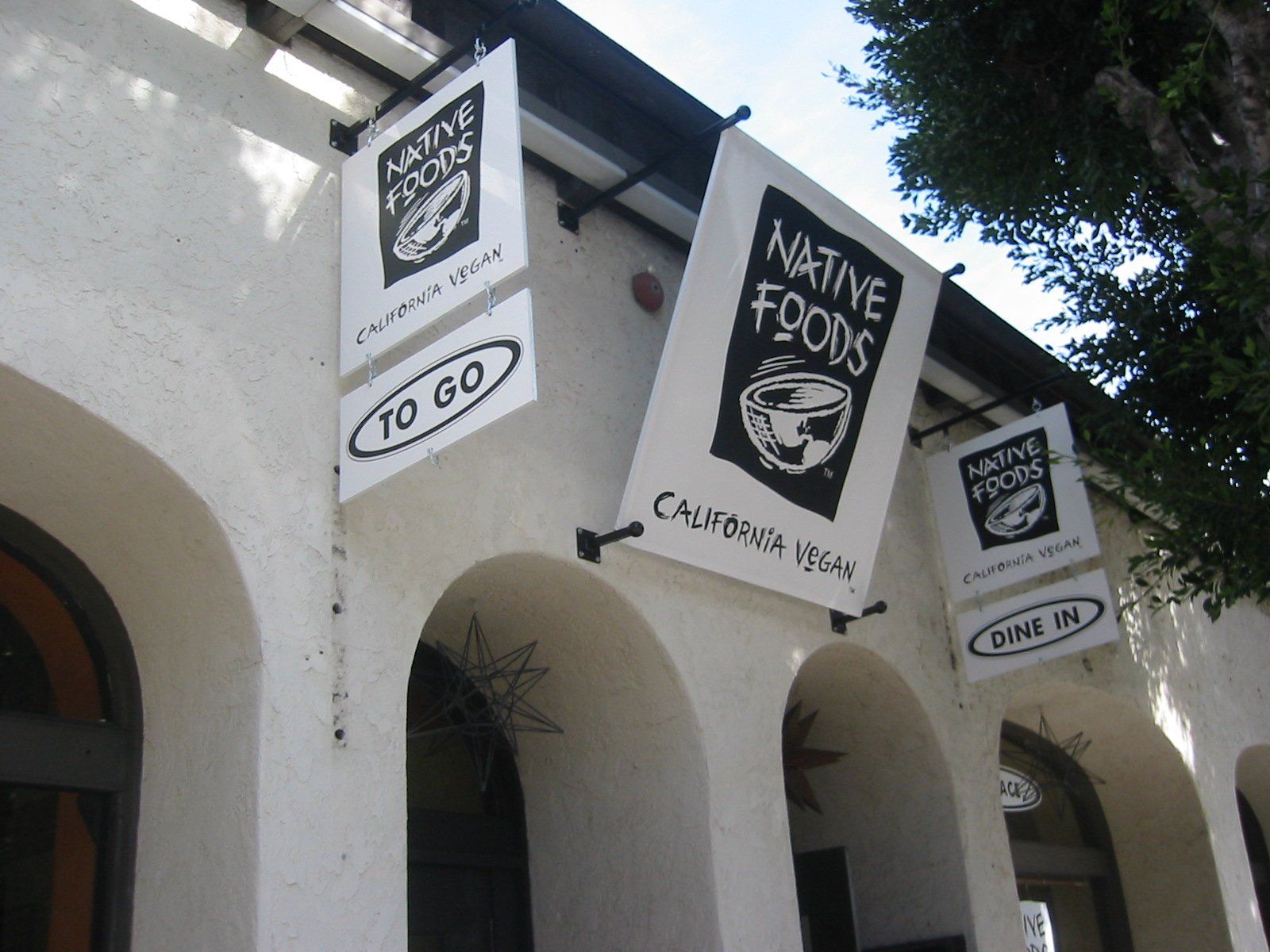 Hanging signs for a Native Foods Cafe above white arches in an outdoor courtyard
