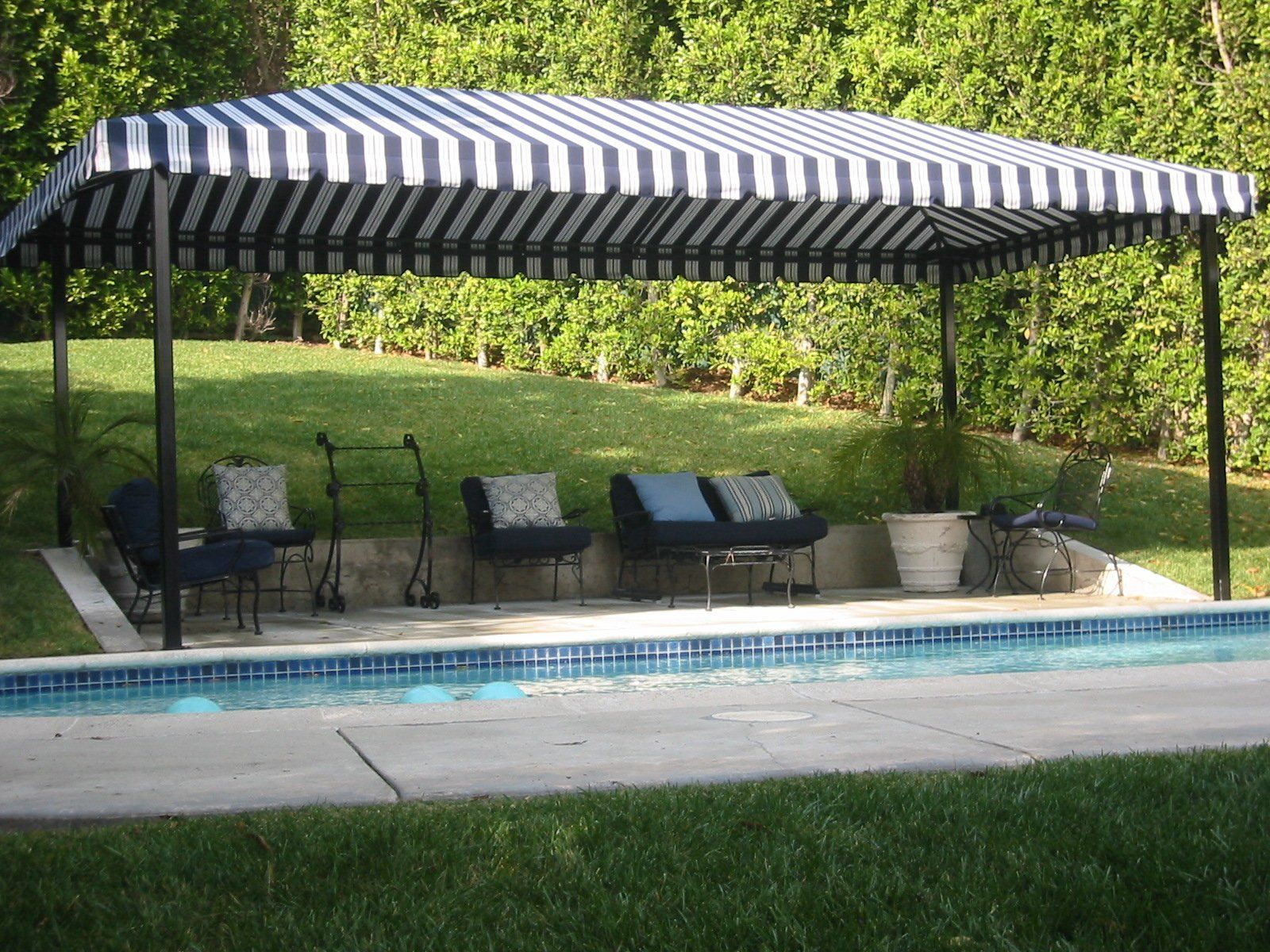 Striped canopy over poolside lounge chairs beside a swimming pool and grassy yard