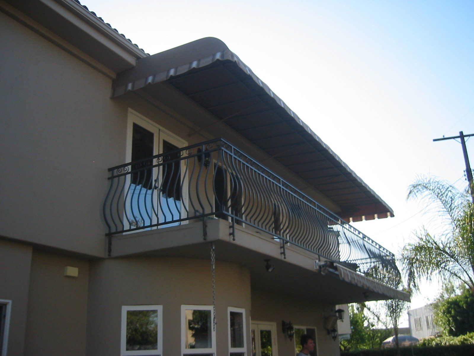 Two-story beige house with a balcony and dark roof, viewed from below in bright sunlight