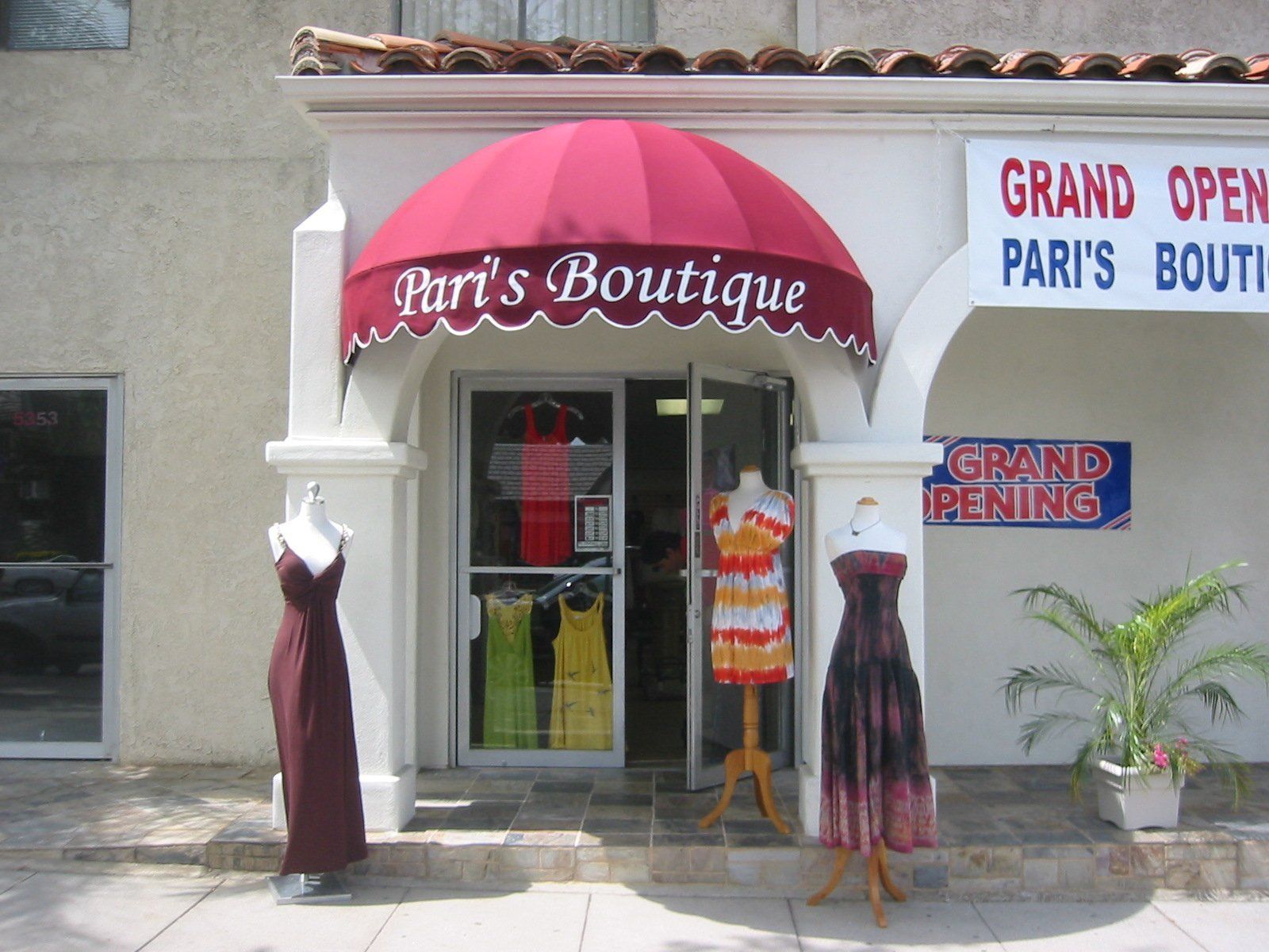 Storefront of Pari’s Boutique with red awning and mannequins outside, plus a grand opening sign
