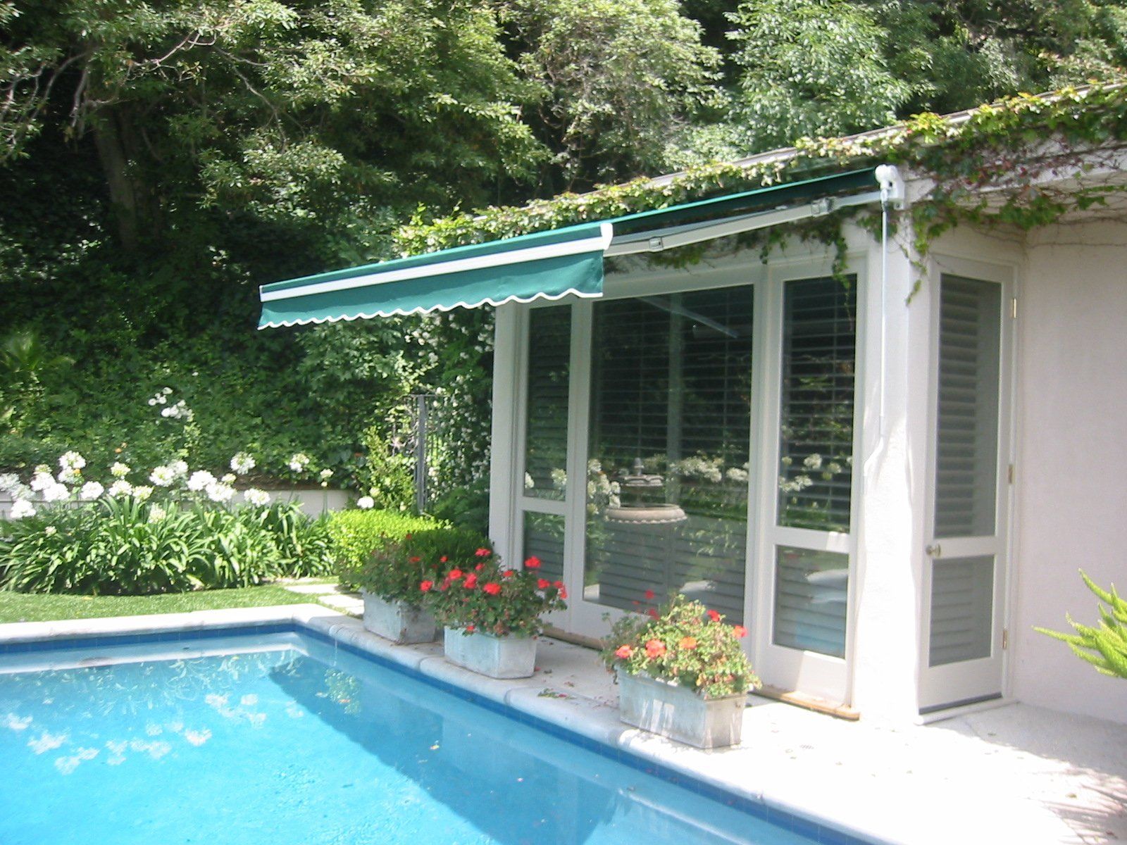 Poolside patio with white columns, teal awning, and flowers beside a blue swimming pool