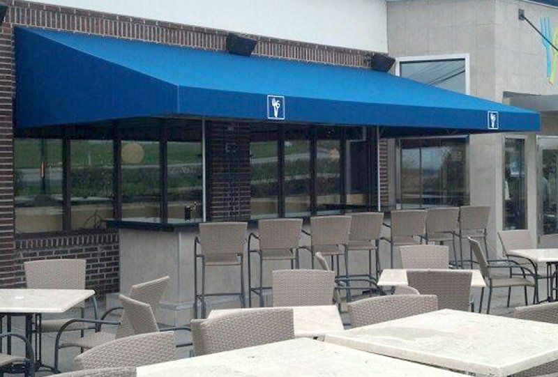 Outdoor patio with tables and chairs outside a building with a blue awning