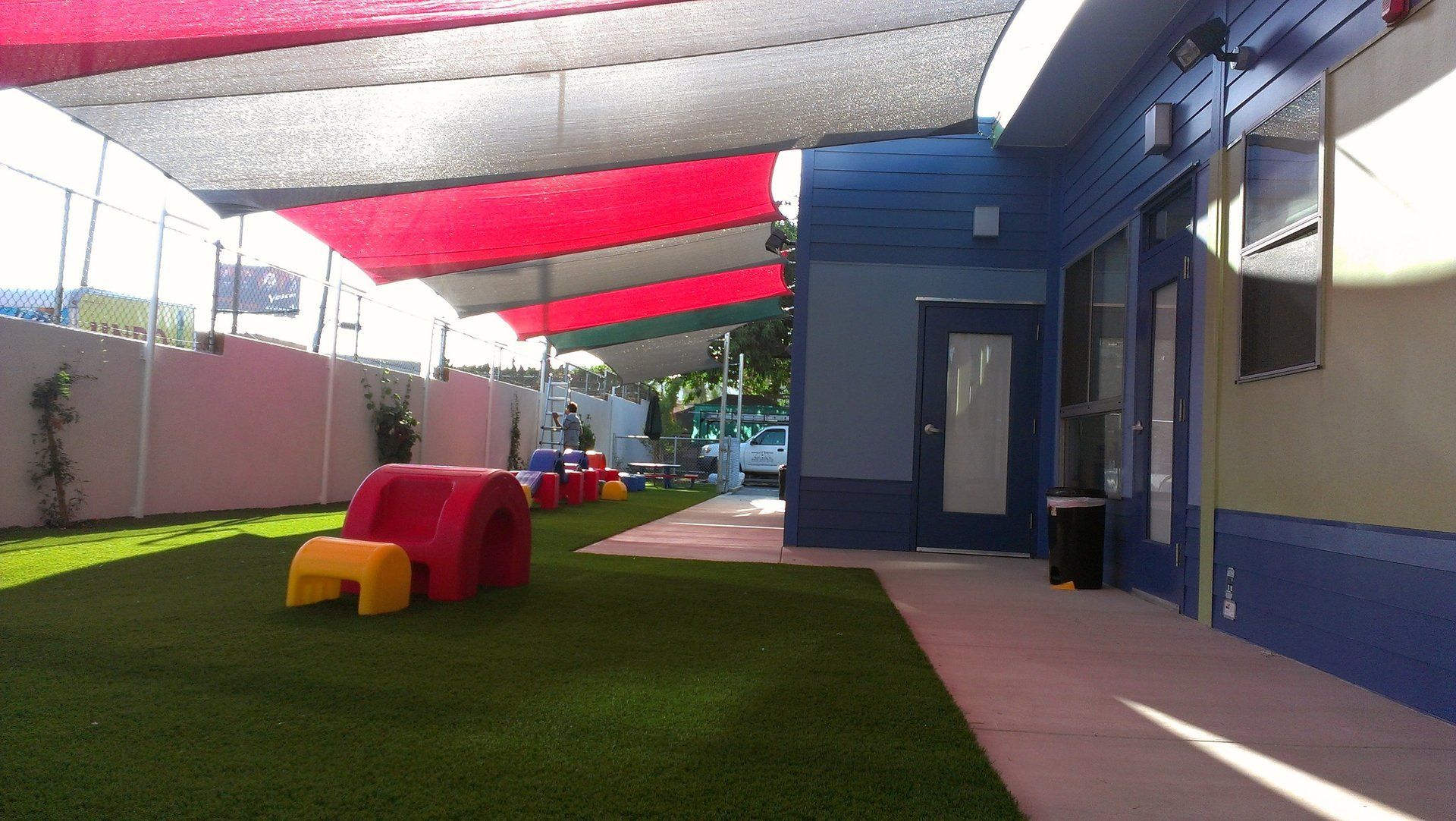 Outdoor playground with colorful canopies, grassy turf, and small play equipment beside a building
