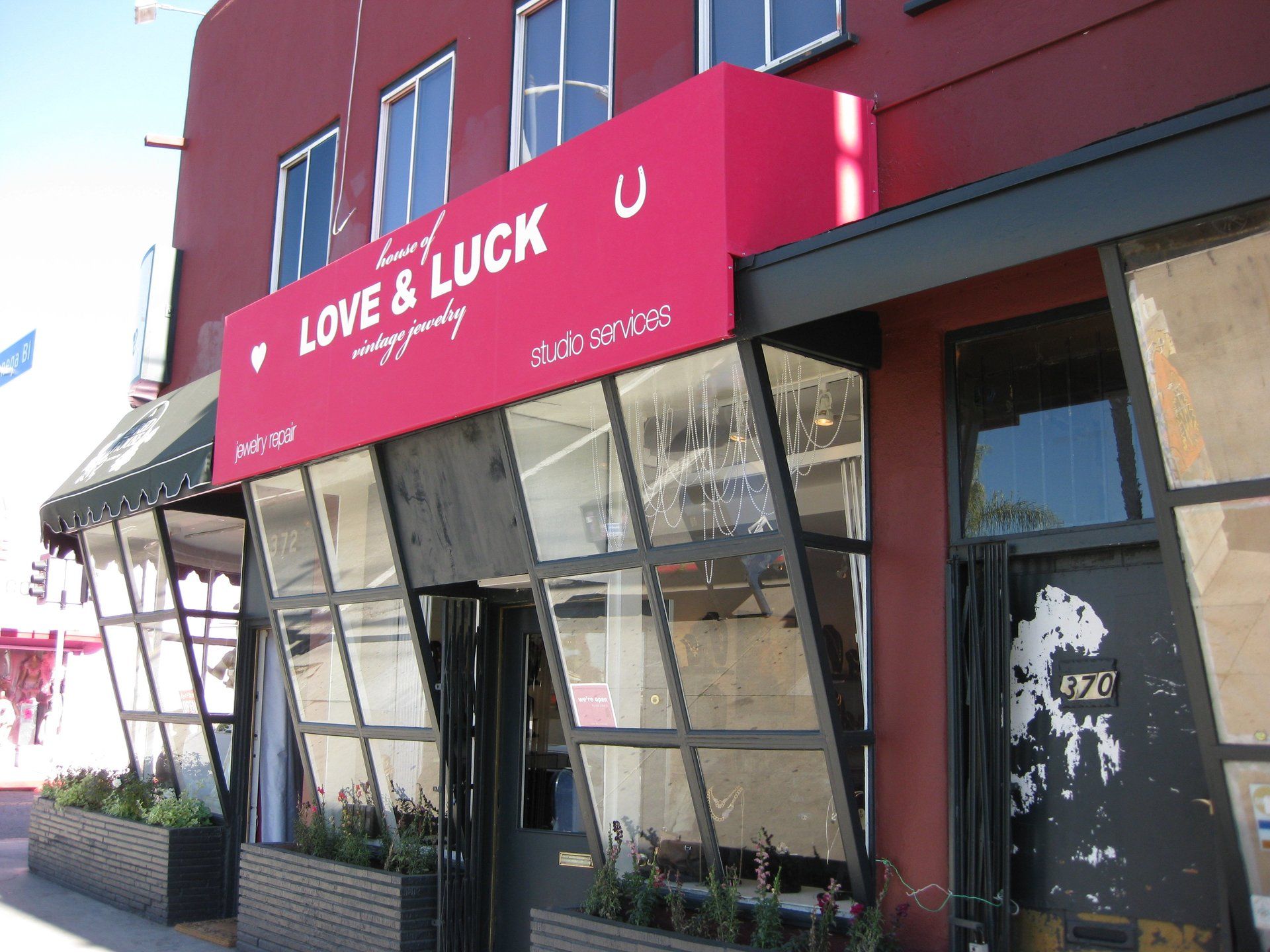 Storefront with a red “LOVE & LUCK” awning and slanted glass windows on a city sidewalk