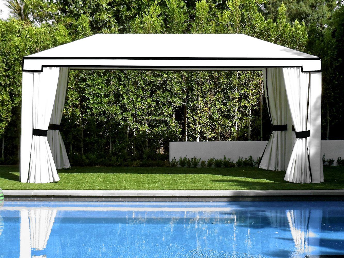 White canopy cabana by a pool, with draped curtains and green trees in the background