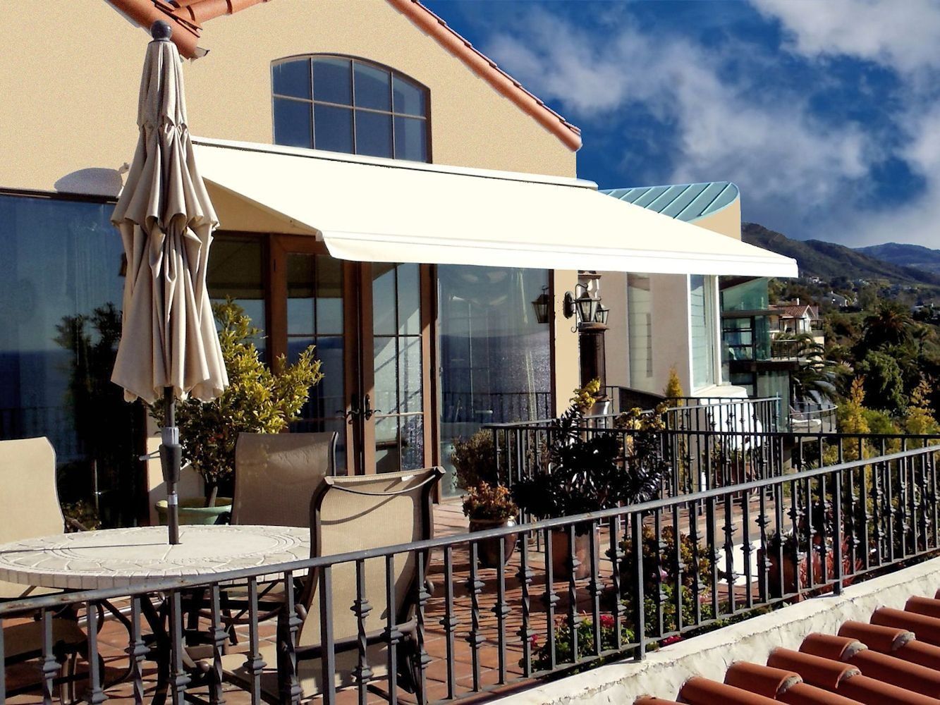 Patio with white awning, closed umbrellas, and black chairs outside a tan building on a sunny day