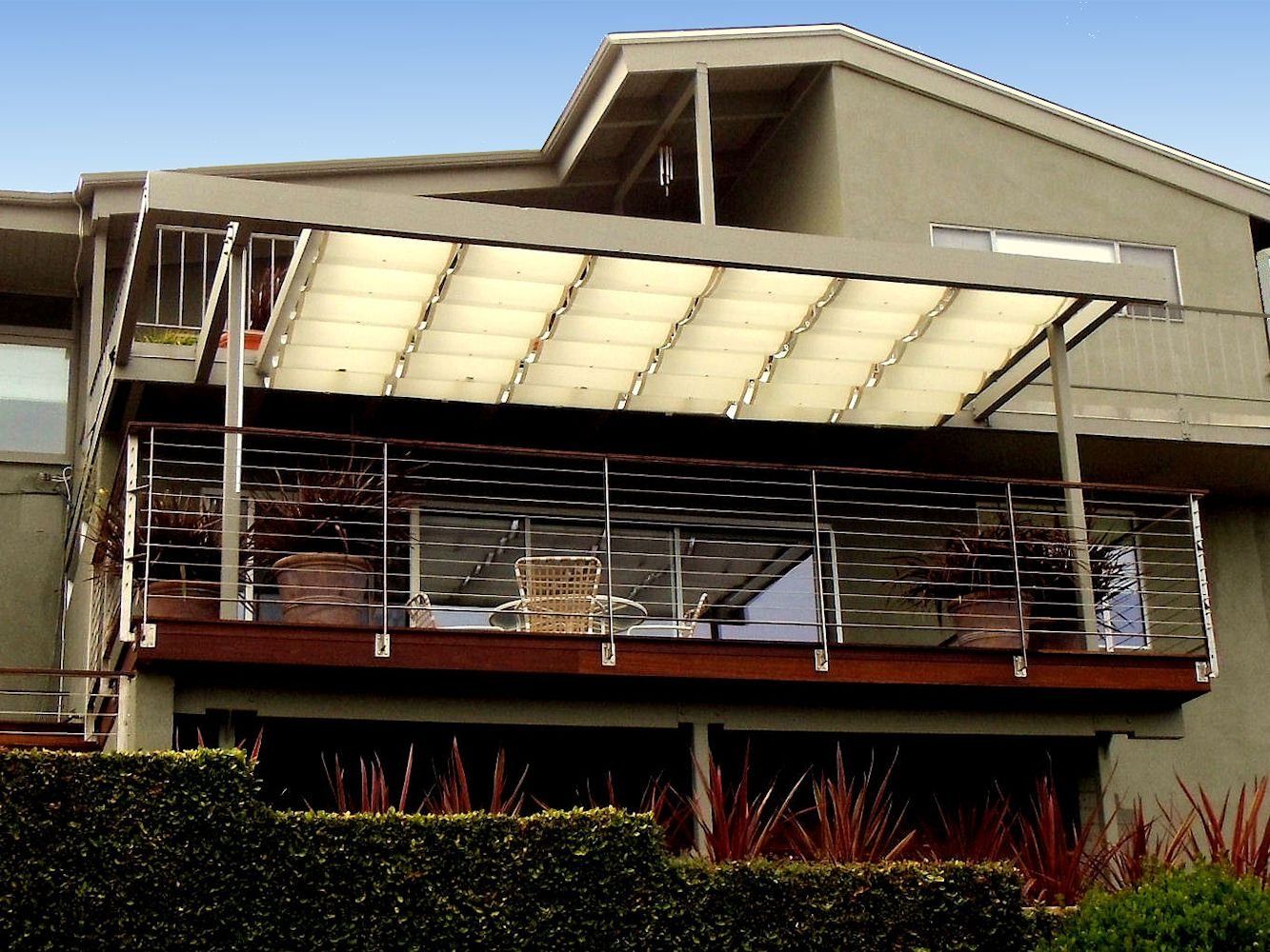 Modern building facade with large white canopy, glass balcony, and landscaped shrubs below