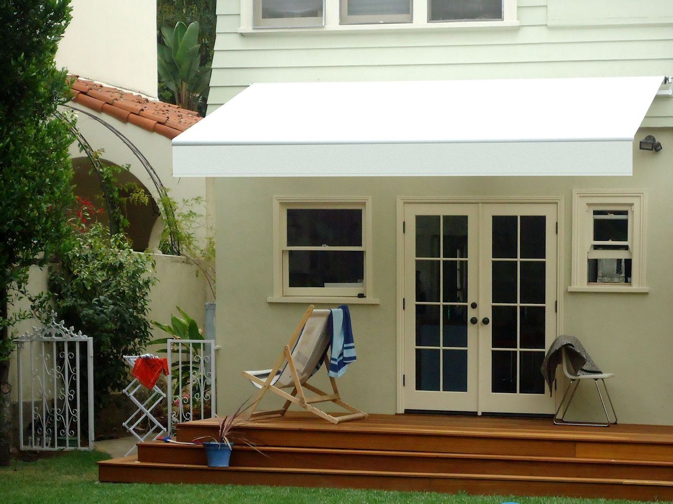 Back patio with white awning, French doors, chairs, and potted plants in a backyard garden.