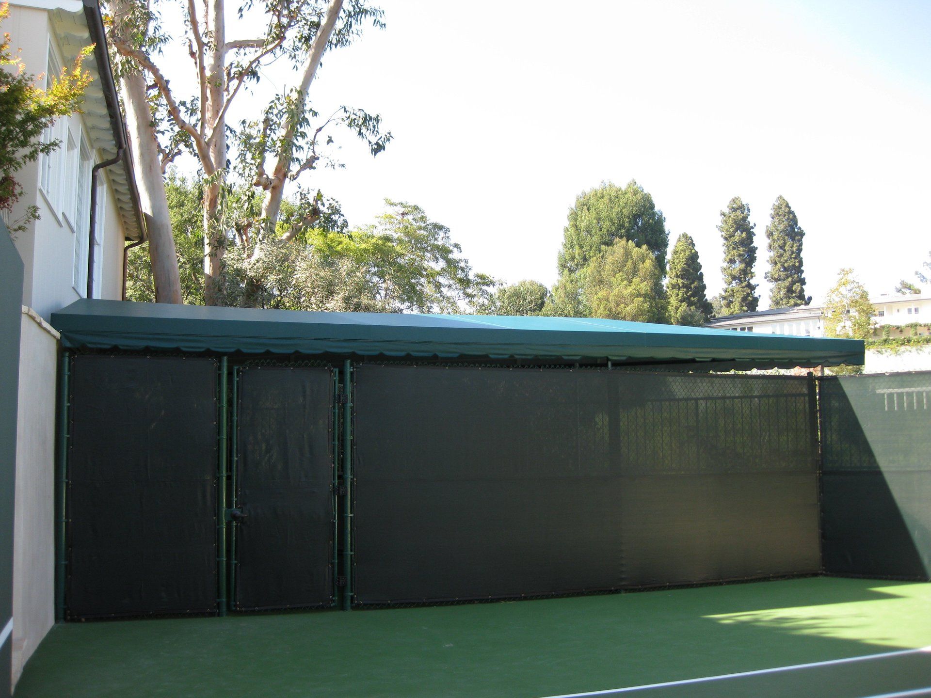 Green-roofed black shed beside a tennis court, with trees in the background