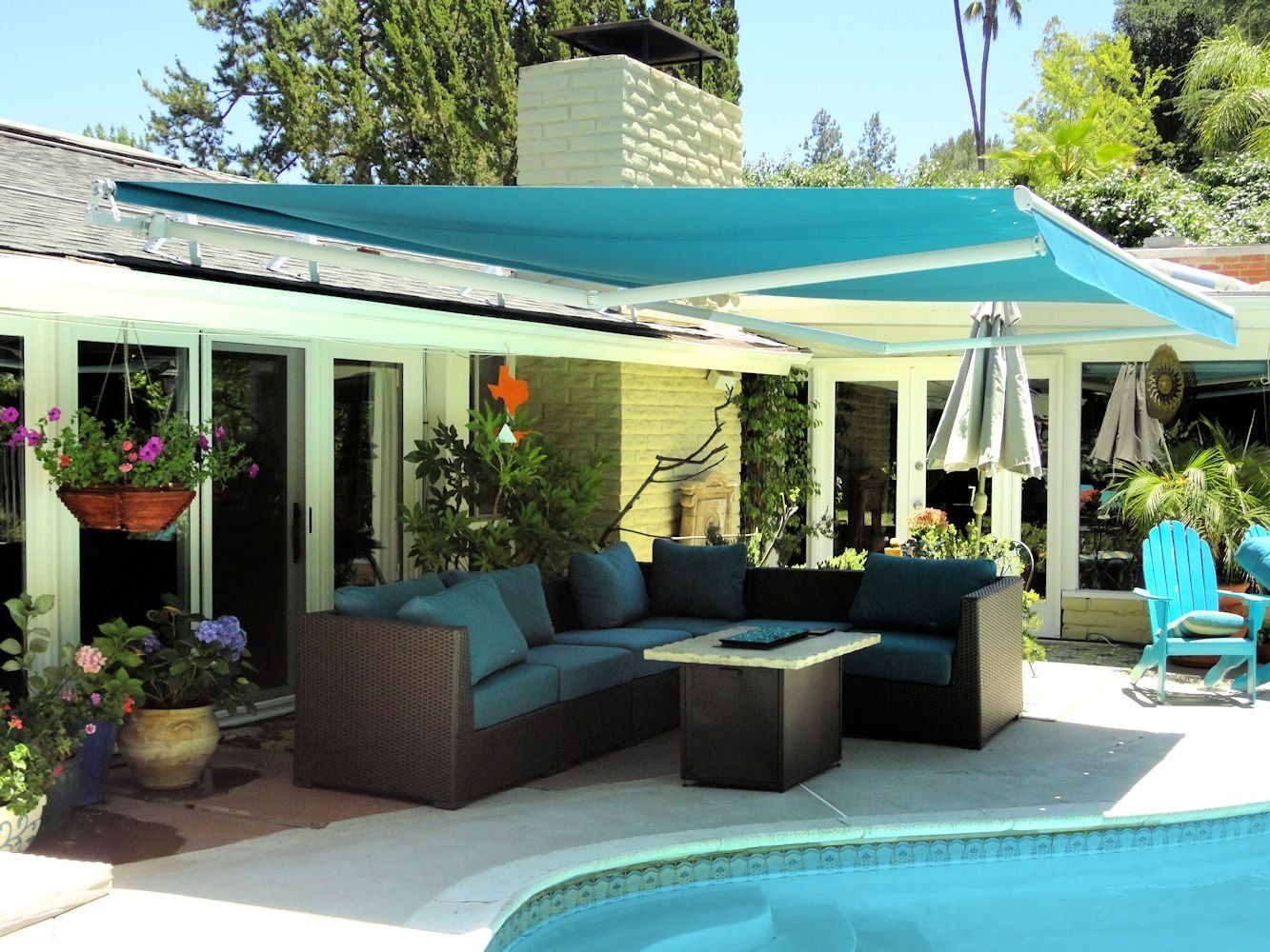 Backyard patio with teal awning, wicker seating, potted plants, and a swimming pool