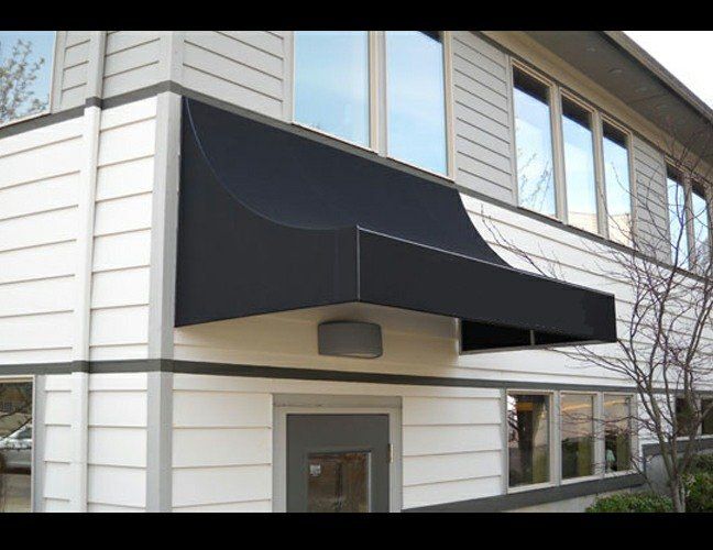 Black awning over an office building entrance with white siding and large windows