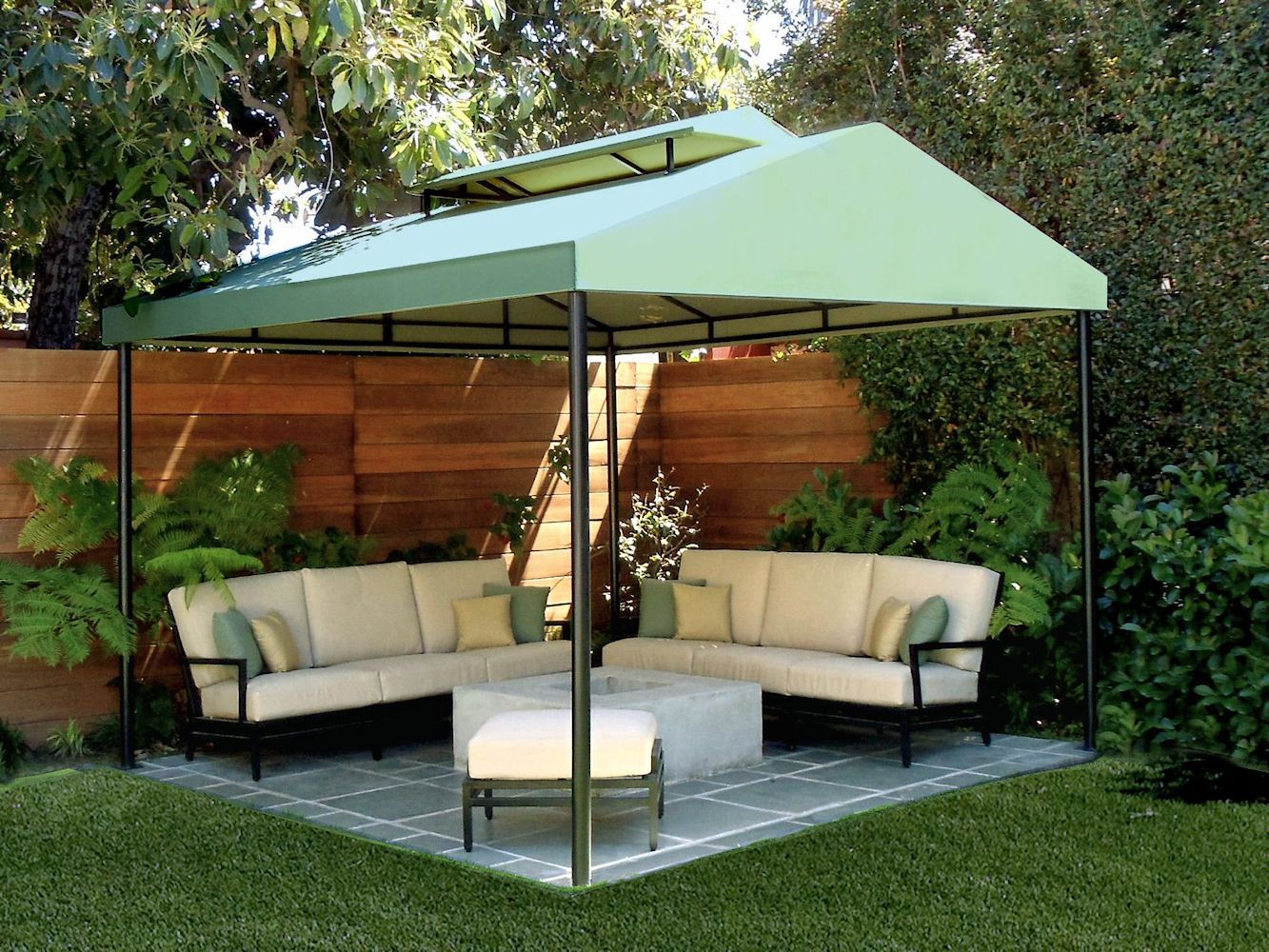 Outdoor patio seating with two beige sofas, a round ottoman, and a green canopy in a fenced backyard