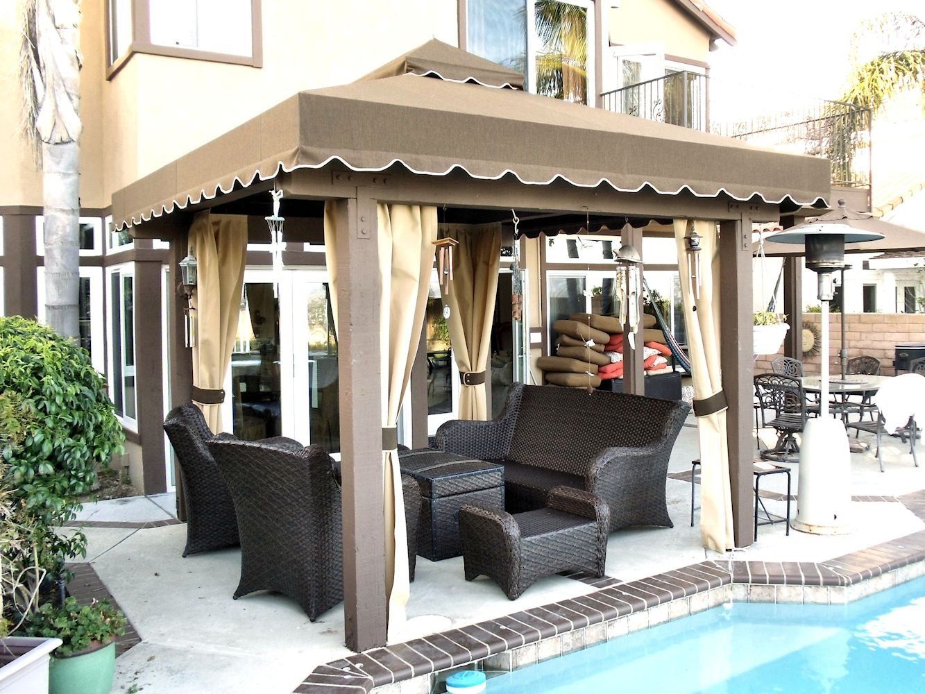 Covered patio lounge beside a swimming pool with wicker chairs and beige curtains