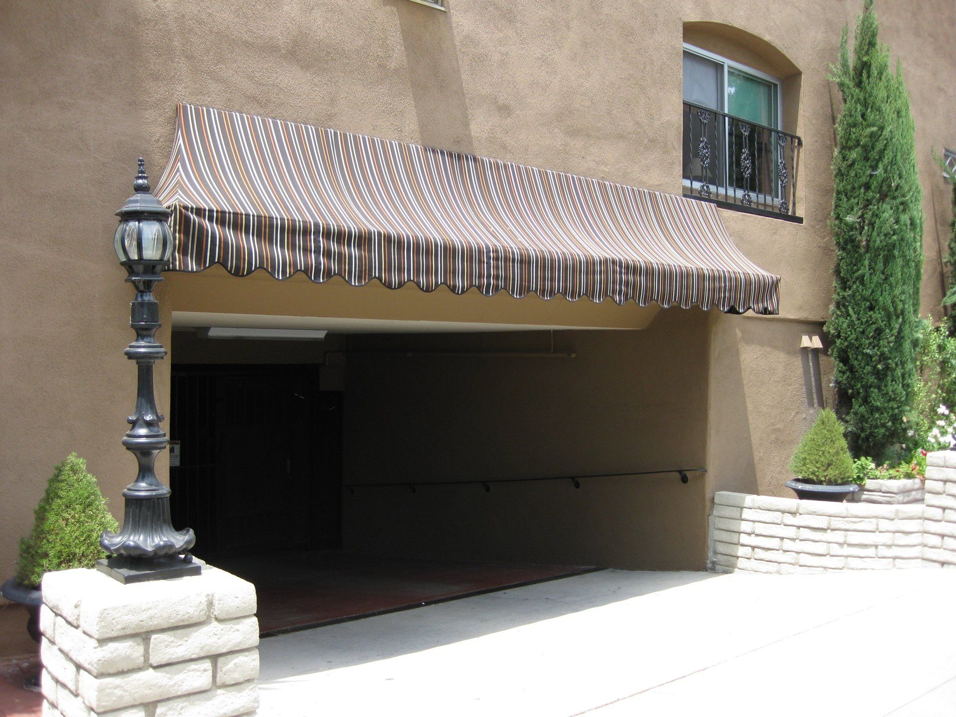 Apartment garage with a striped awning, lamp post, and landscaped stone planters