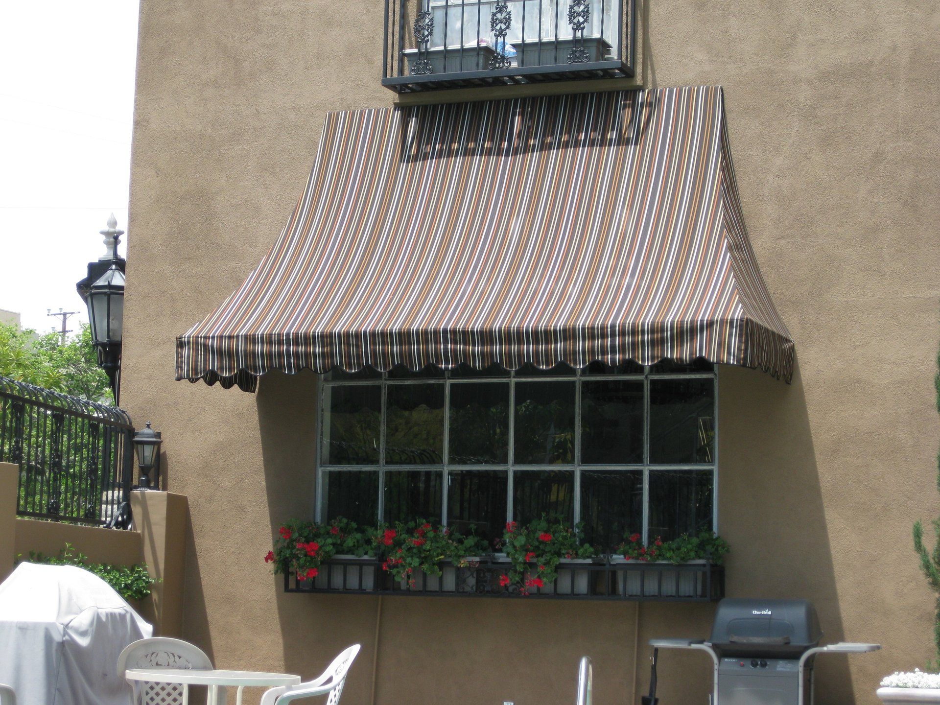 Striped awning over a window box on a stucco building patio with chairs and outdoor furniture