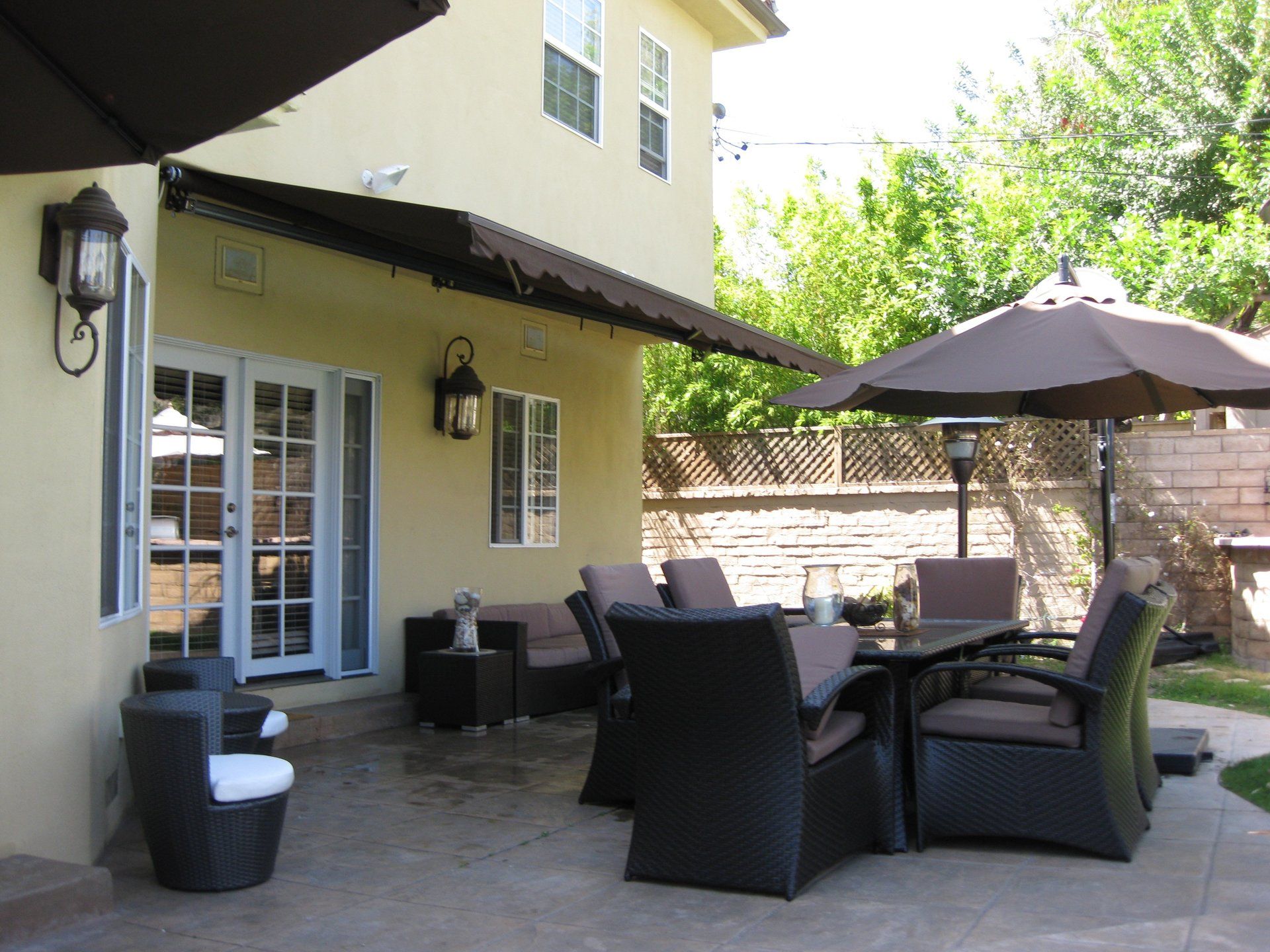 Patio with wicker chairs, table, and umbrella beside a house with French doors