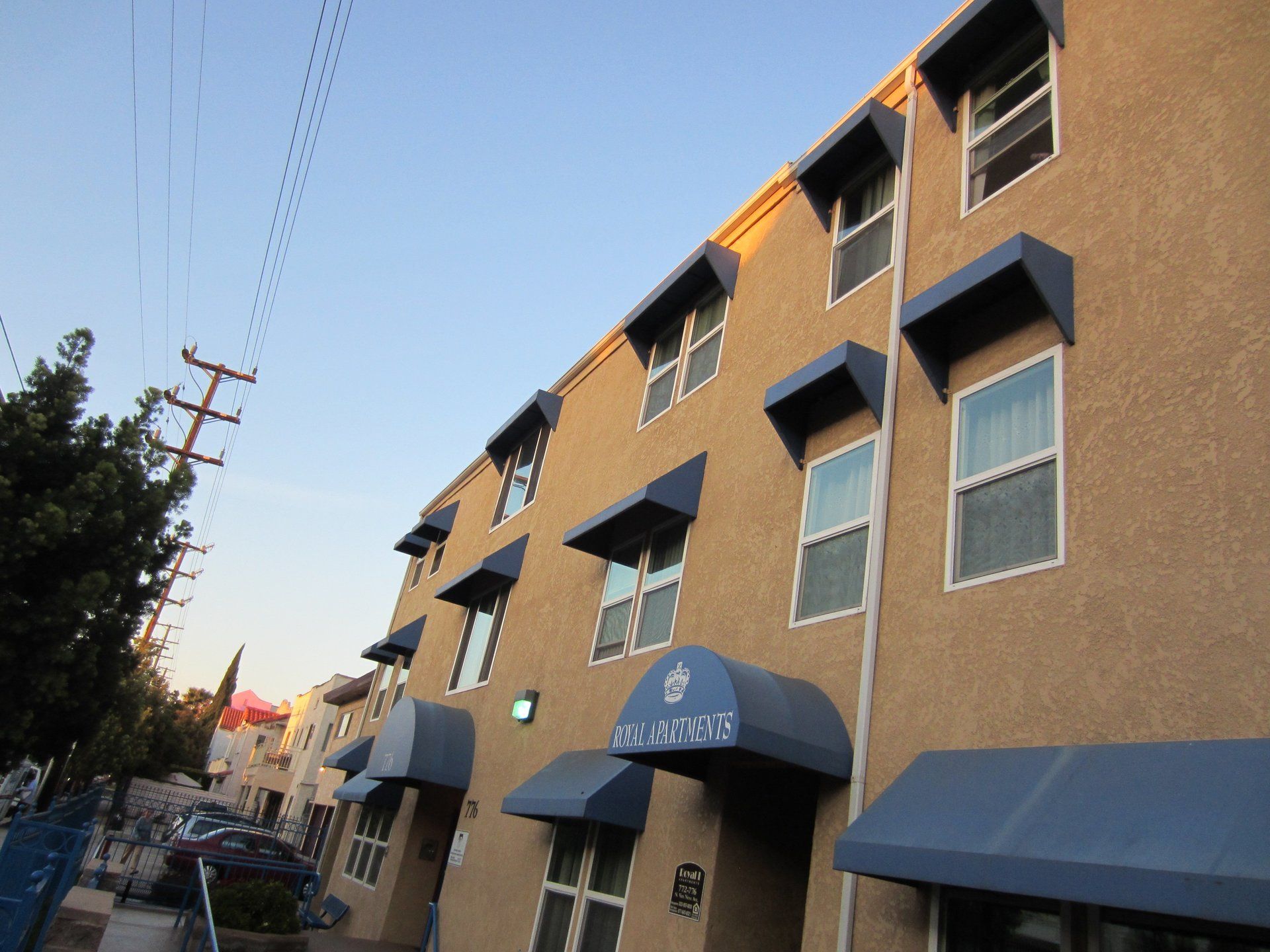 Brick apartment building with blue awnings along a sidewalk at dusk