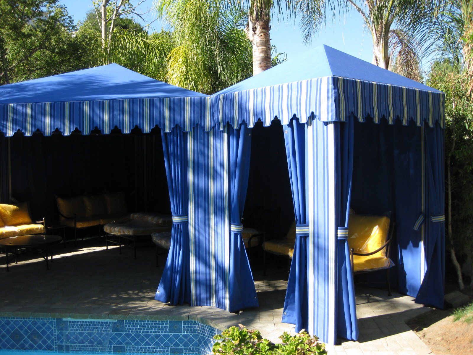 Blue striped canopy tent with open drapes and yellow chairs in a sunny outdoor area