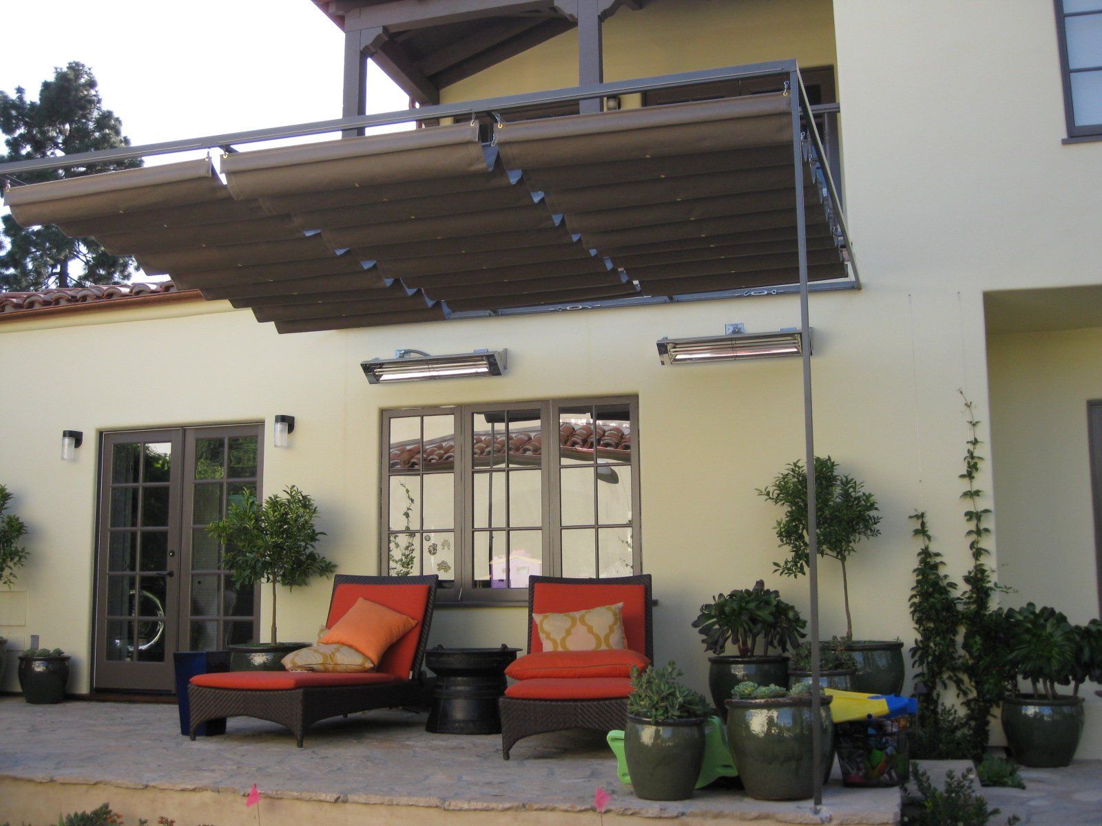 Patio with two orange lounge chairs, potted plants, and a retractable awning against a cream house