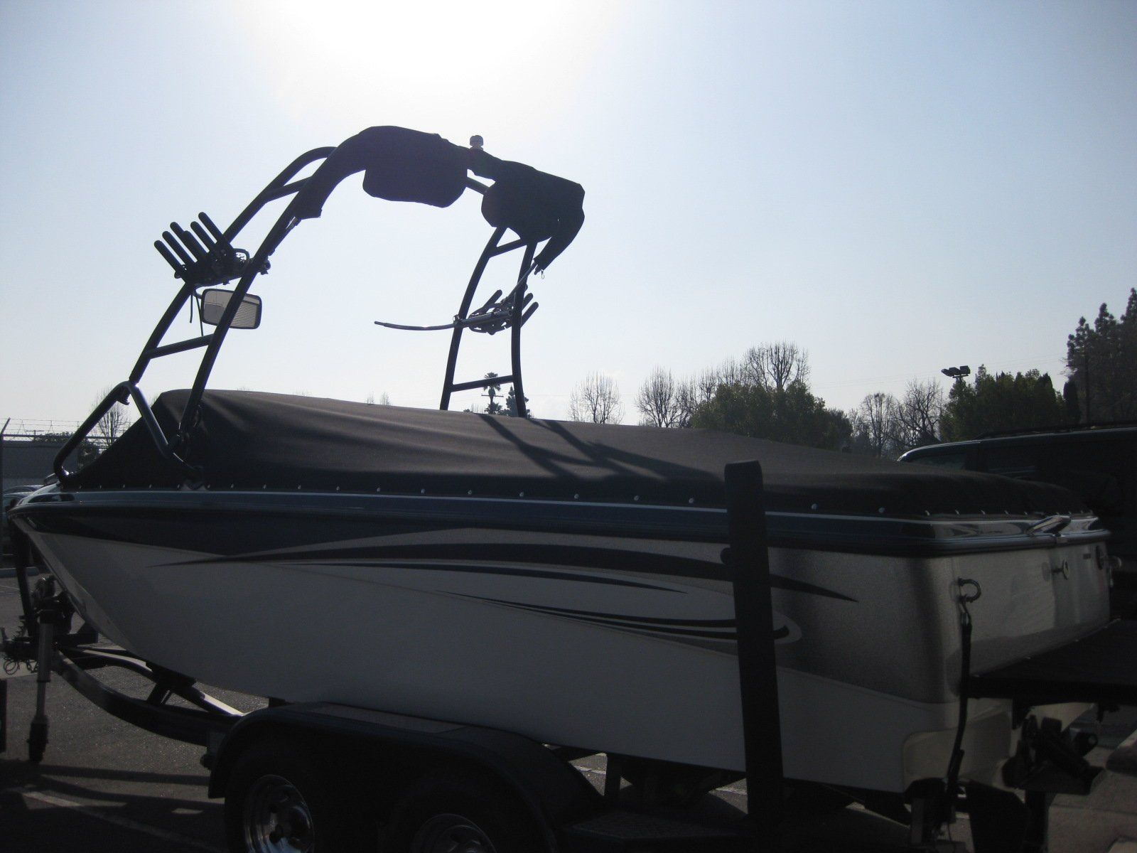 White boat on trailer with black wakeboard tower, silhouetted against a bright sky outdoors