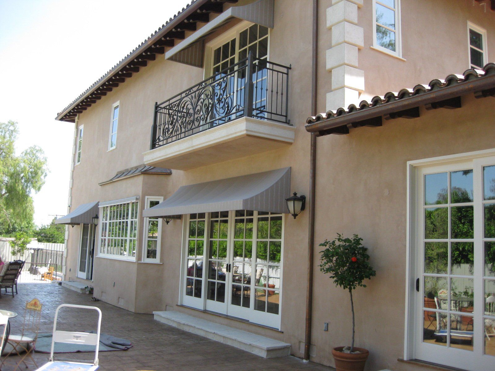 Patio of a beige stucco house with French doors, balcony, awning, and potted tree