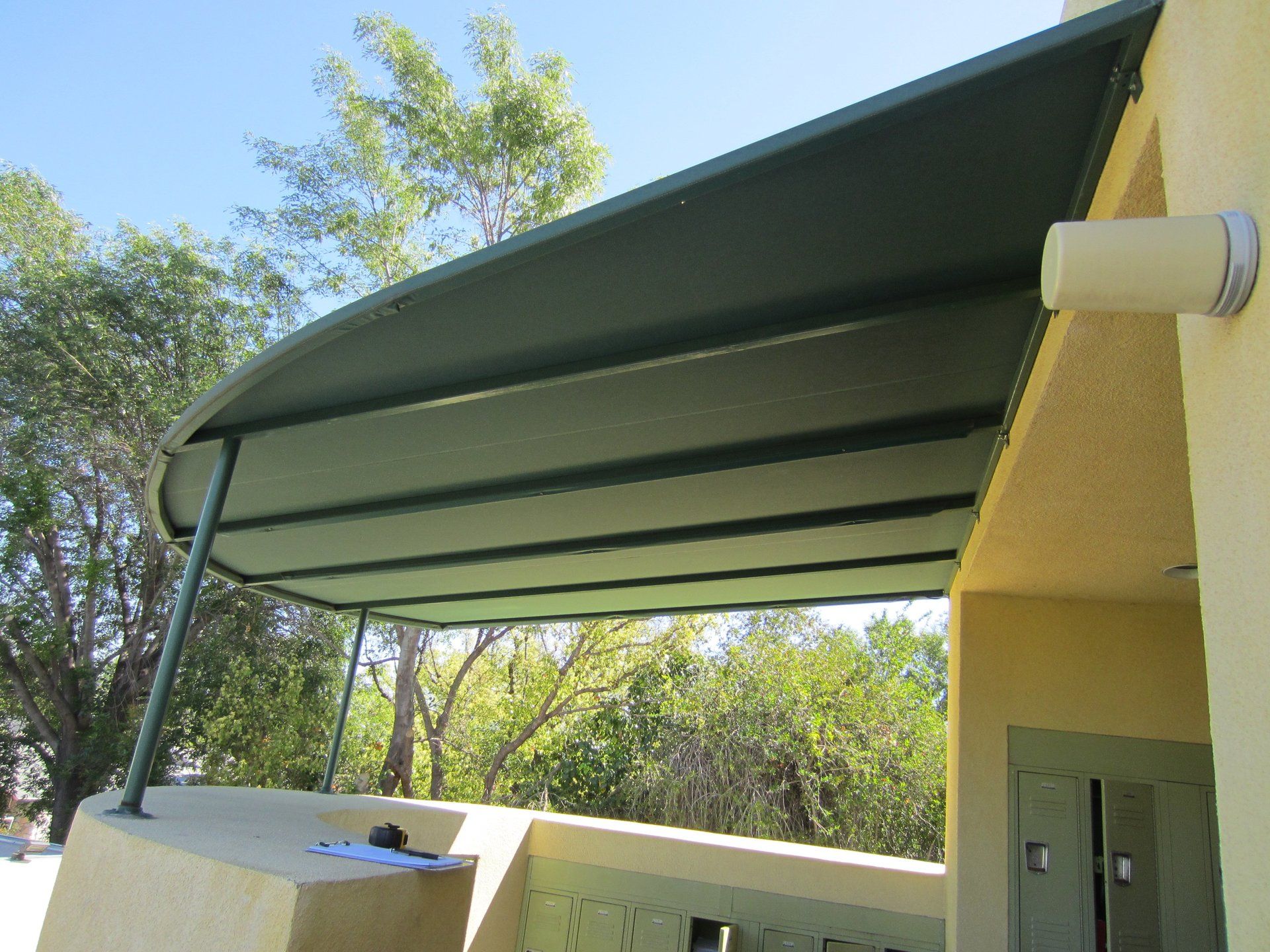 Green awning over a patio beside a yellow building, with trees in the background.