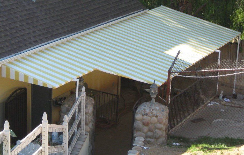 Yellow-and-white striped awning over a patio beside a brick house and fenced yard