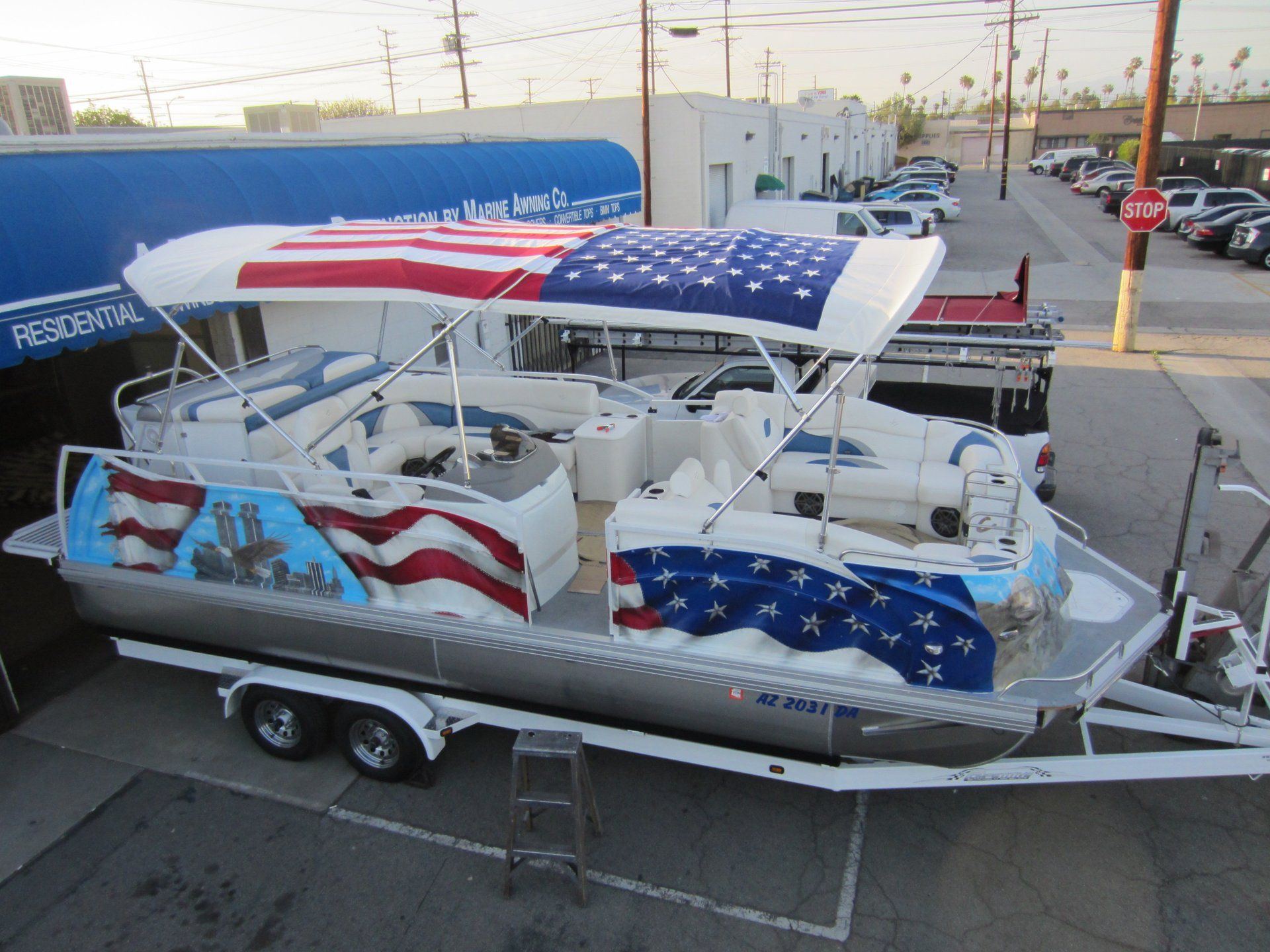 Patriotic-themed pontoon boat on a trailer with red, white, and blue flag graphics outdoors.