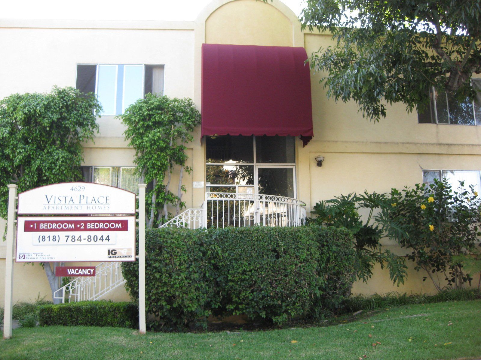 Sign for a veterinary office in front of a beige building with maroon awning and hedges.