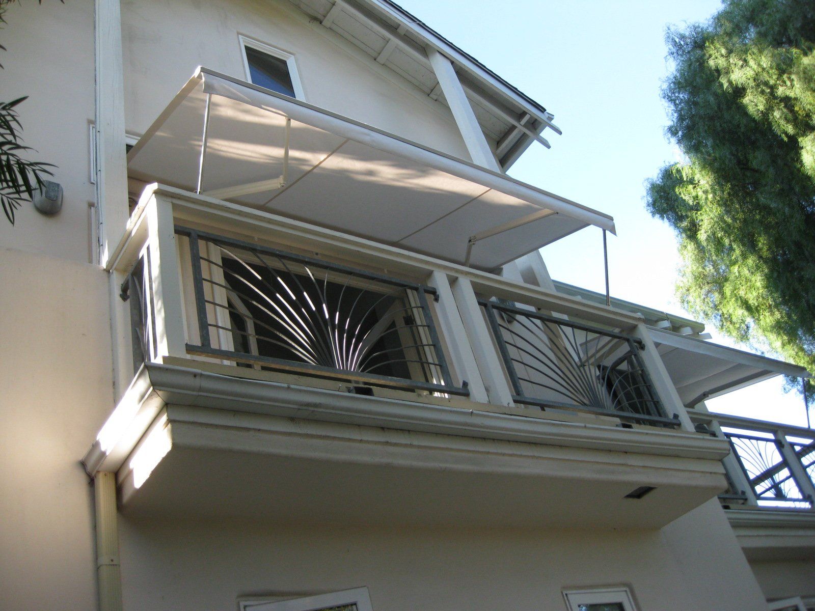 Exterior of a white apartment building with balconies and awnings, viewed from below against blue sky