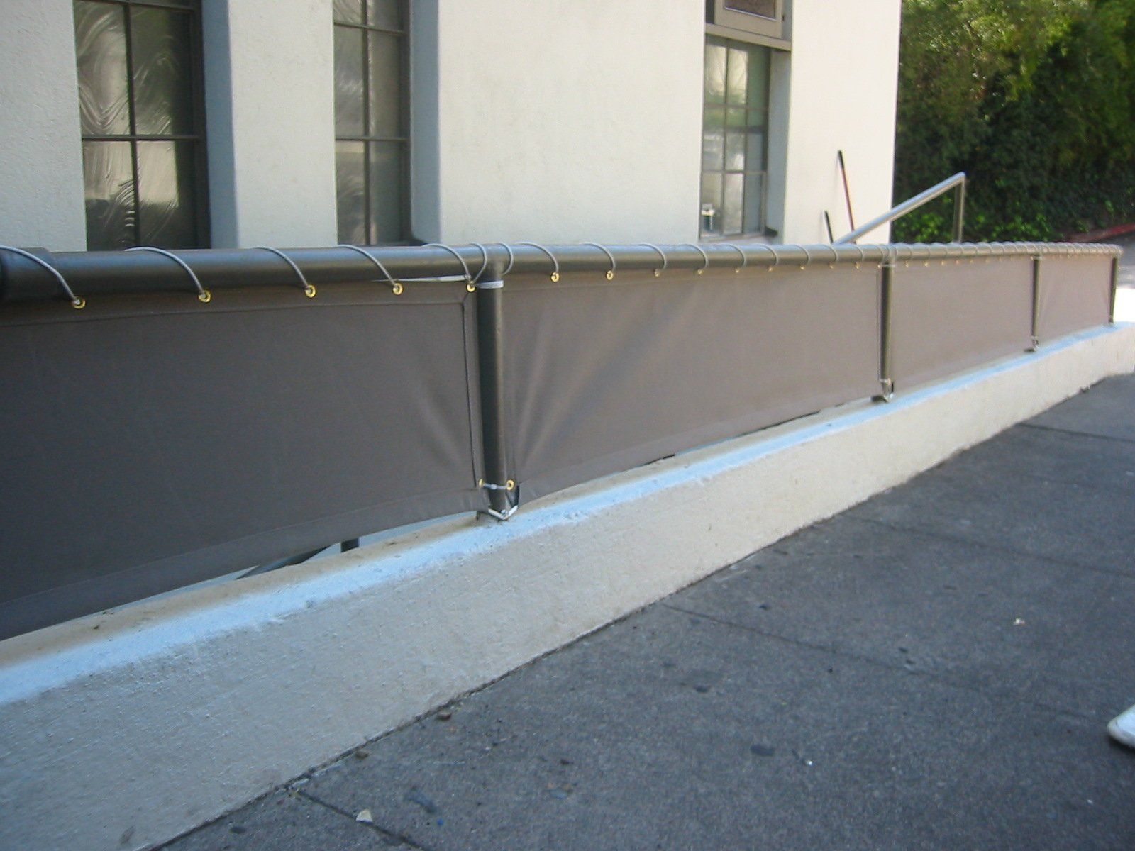 Outdoor walkway beside a building with a gray railing and concrete curb along the pavement