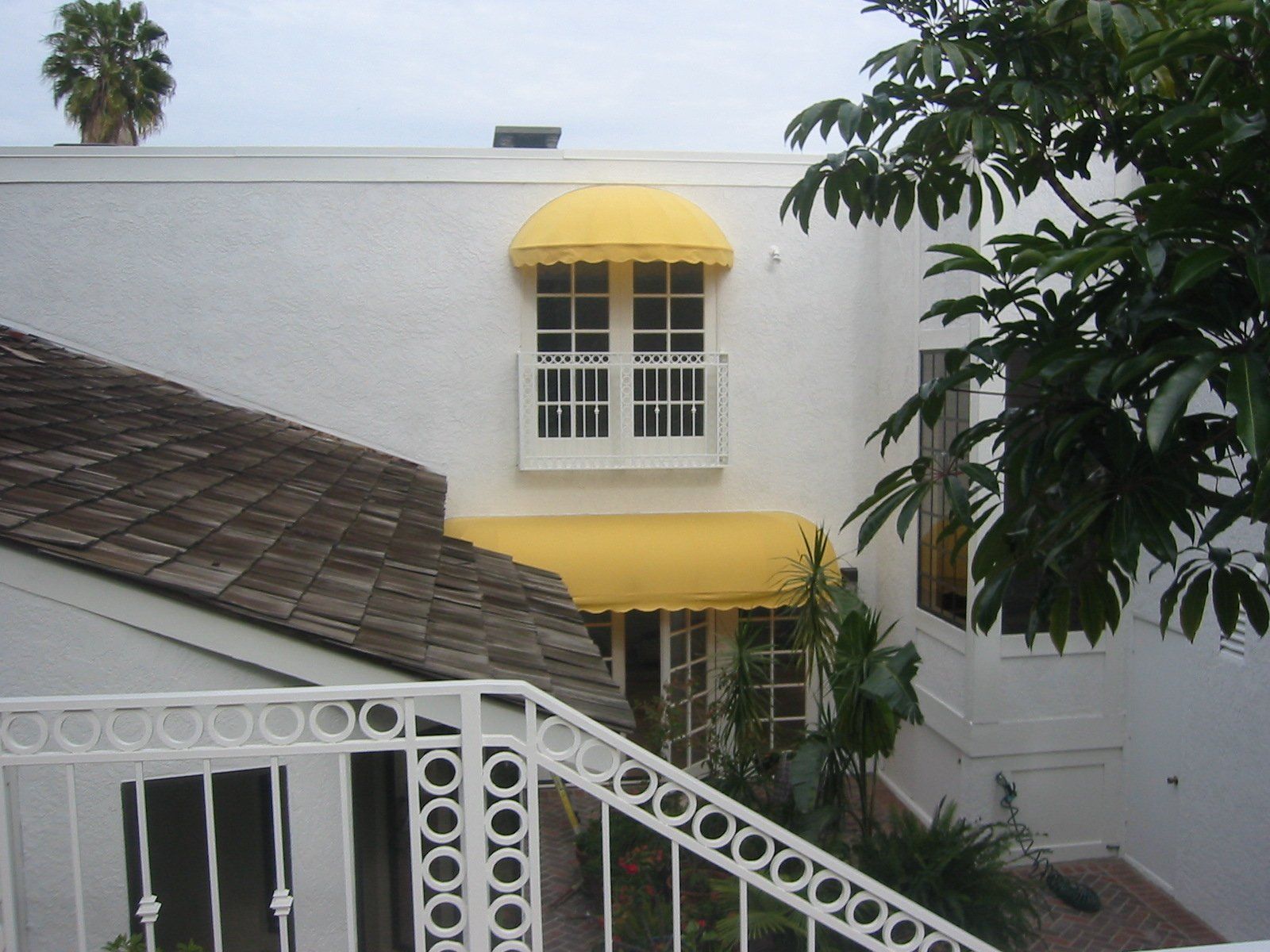 White house exterior with yellow awnings, white railing, and palm trees above a tiled roof