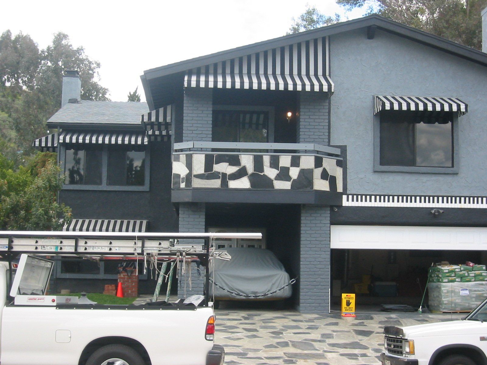Two-story house with black-and-white striped awnings and a white utility van parked in front