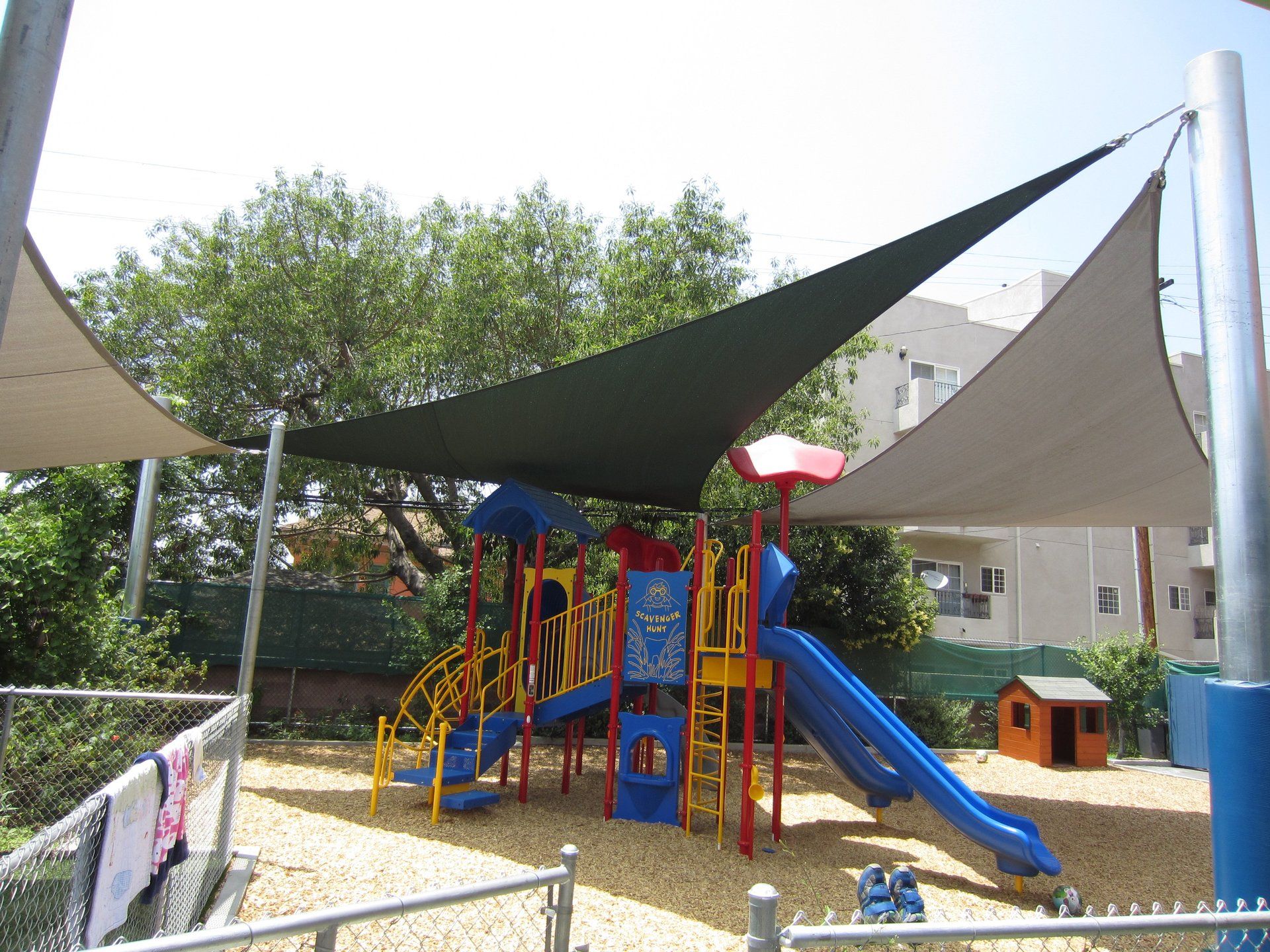 Colorful playground with blue slide, climbing structure, and sunshade sails on a gravel surface