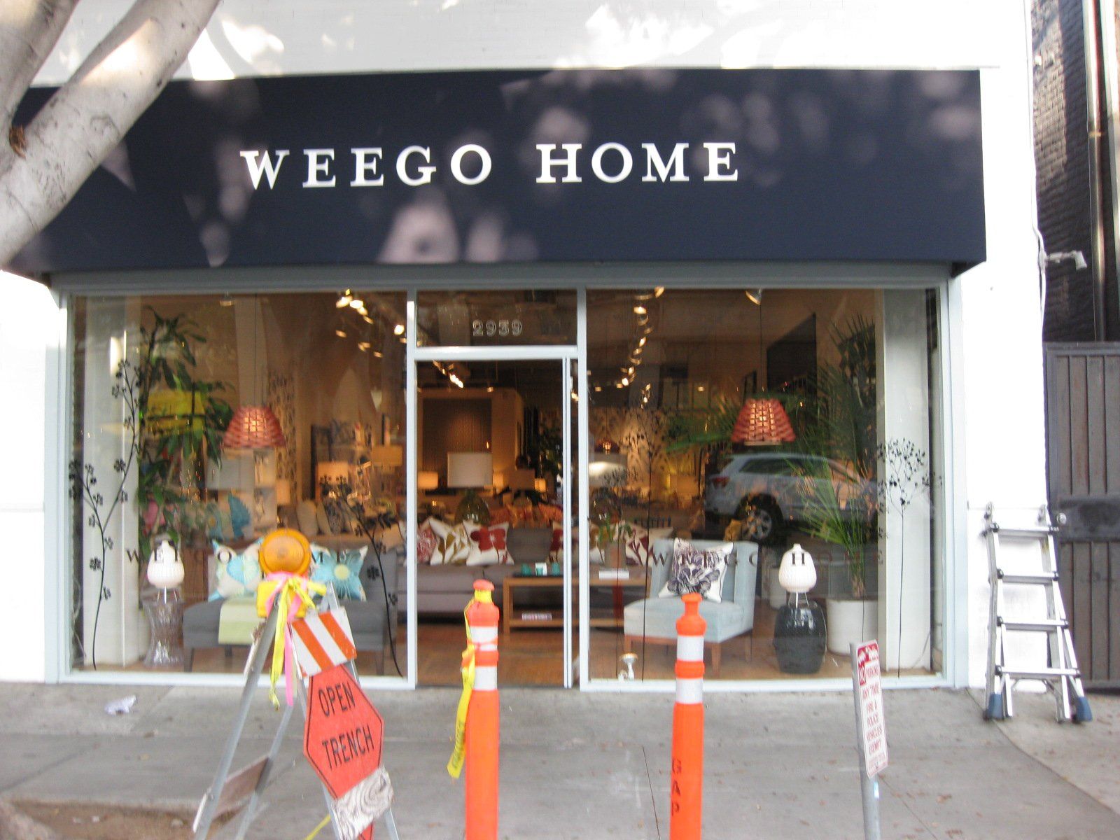 Storefront of WEEGO HOME with glass entrance, plants in the window, and orange traffic cones outside