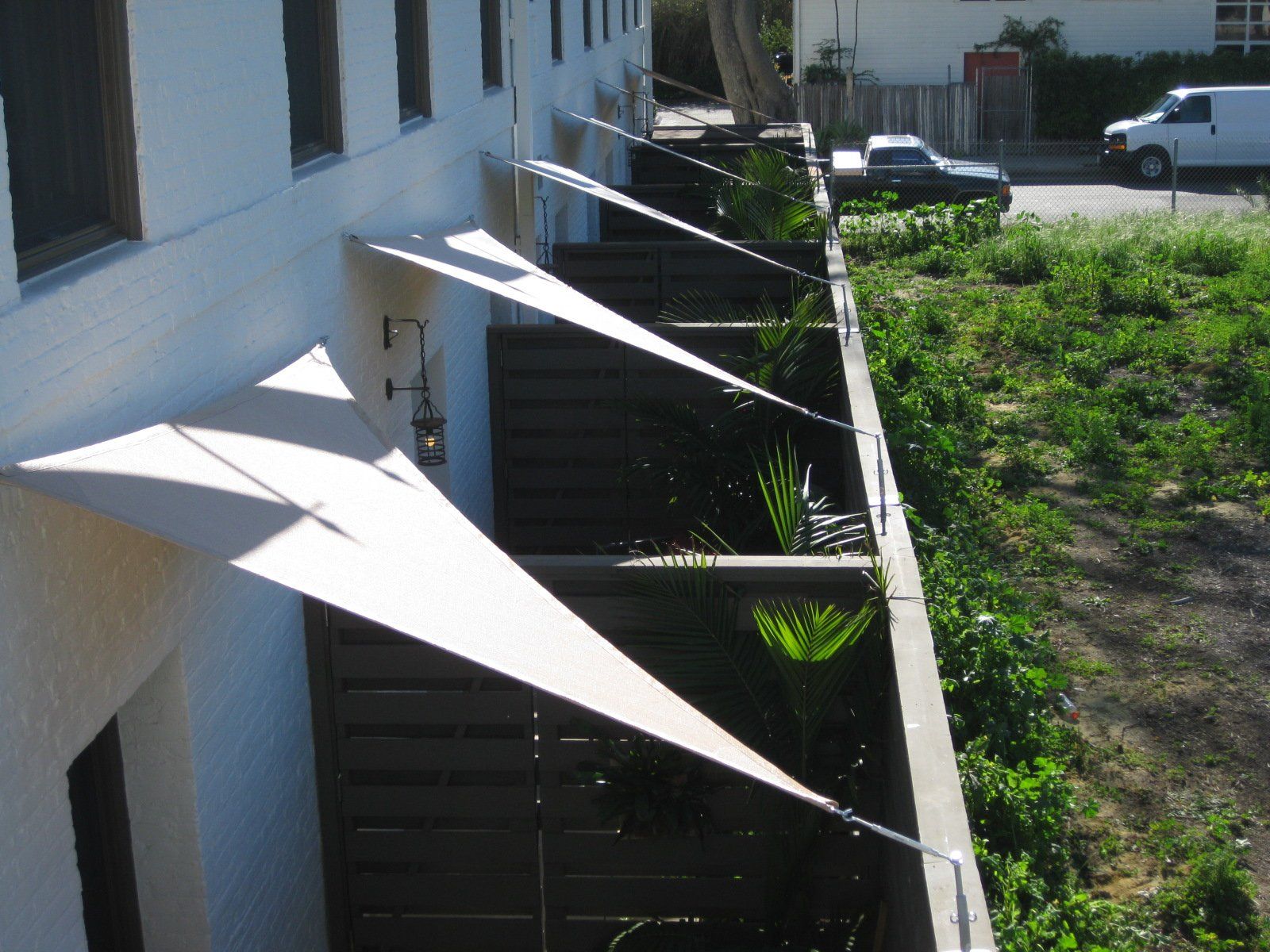 White building wall with several white awnings shading a staircase beside a grassy yard.