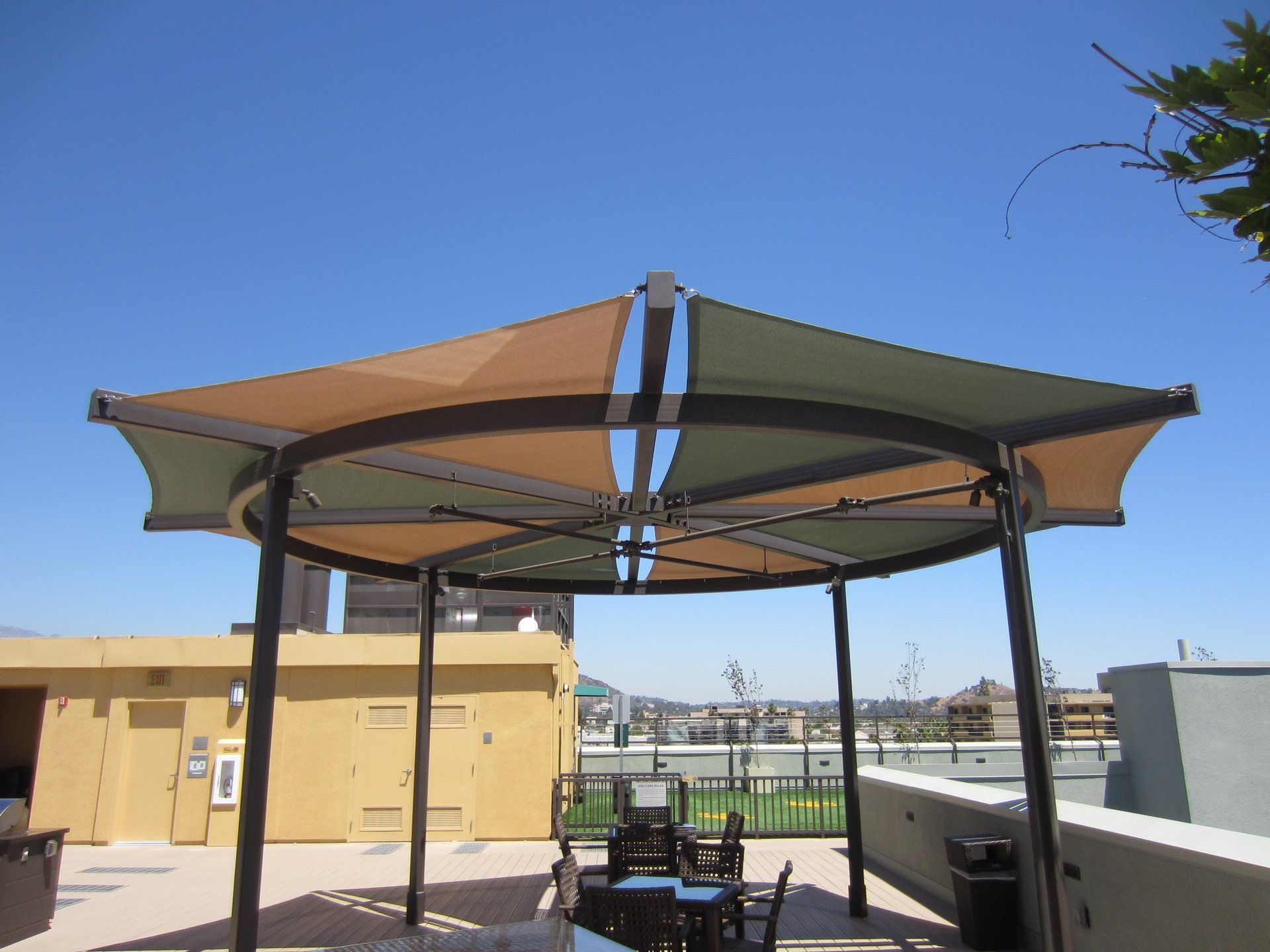 Outdoor shaded patio with a tan canopy and black metal frame overlooking a rooftop terrace.