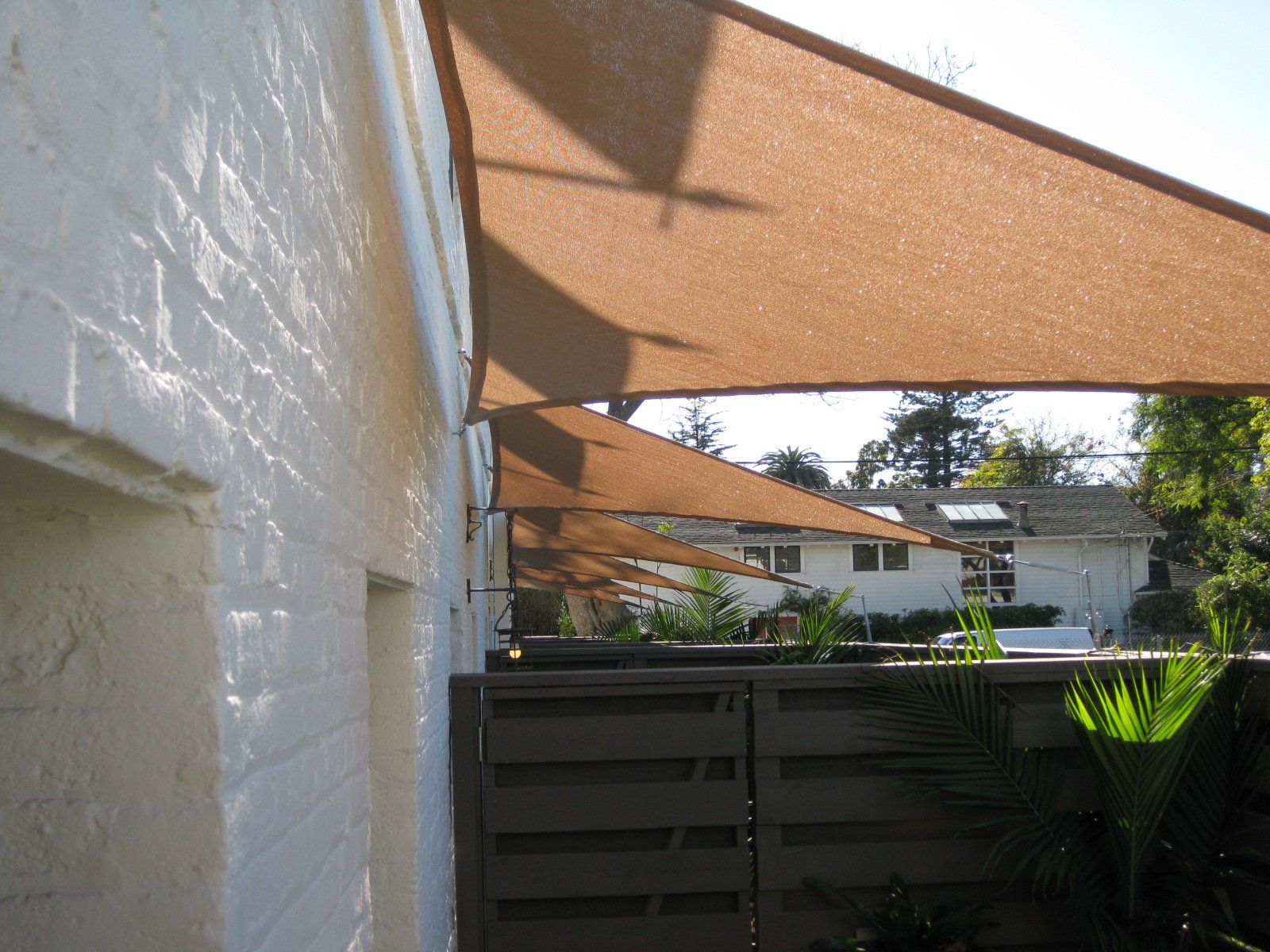 Patio with tan shade sails over a fenced backyard and neighboring house in daylight