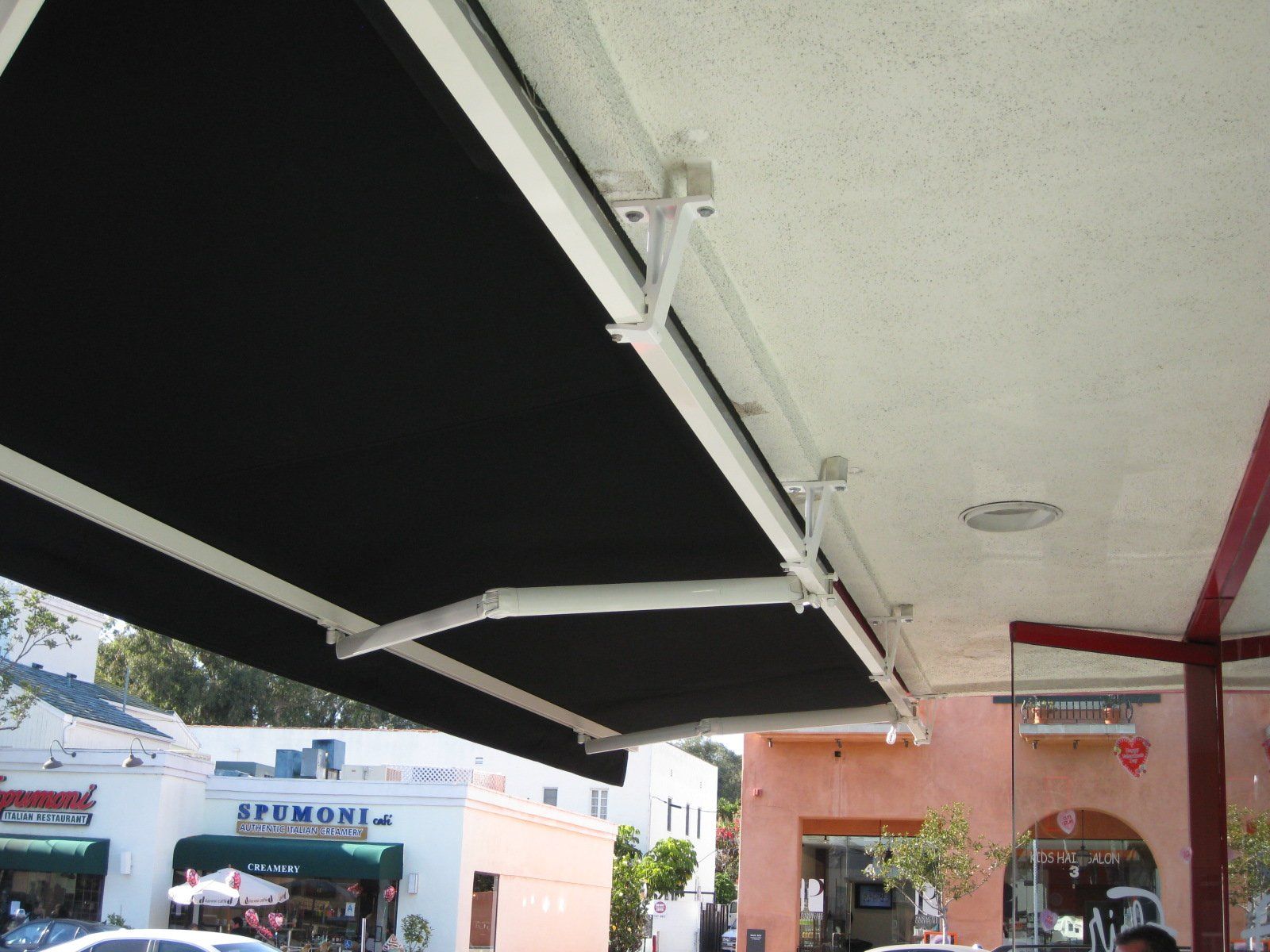 Black awning extended over a storefront walkway near parked cars and a peach-colored building