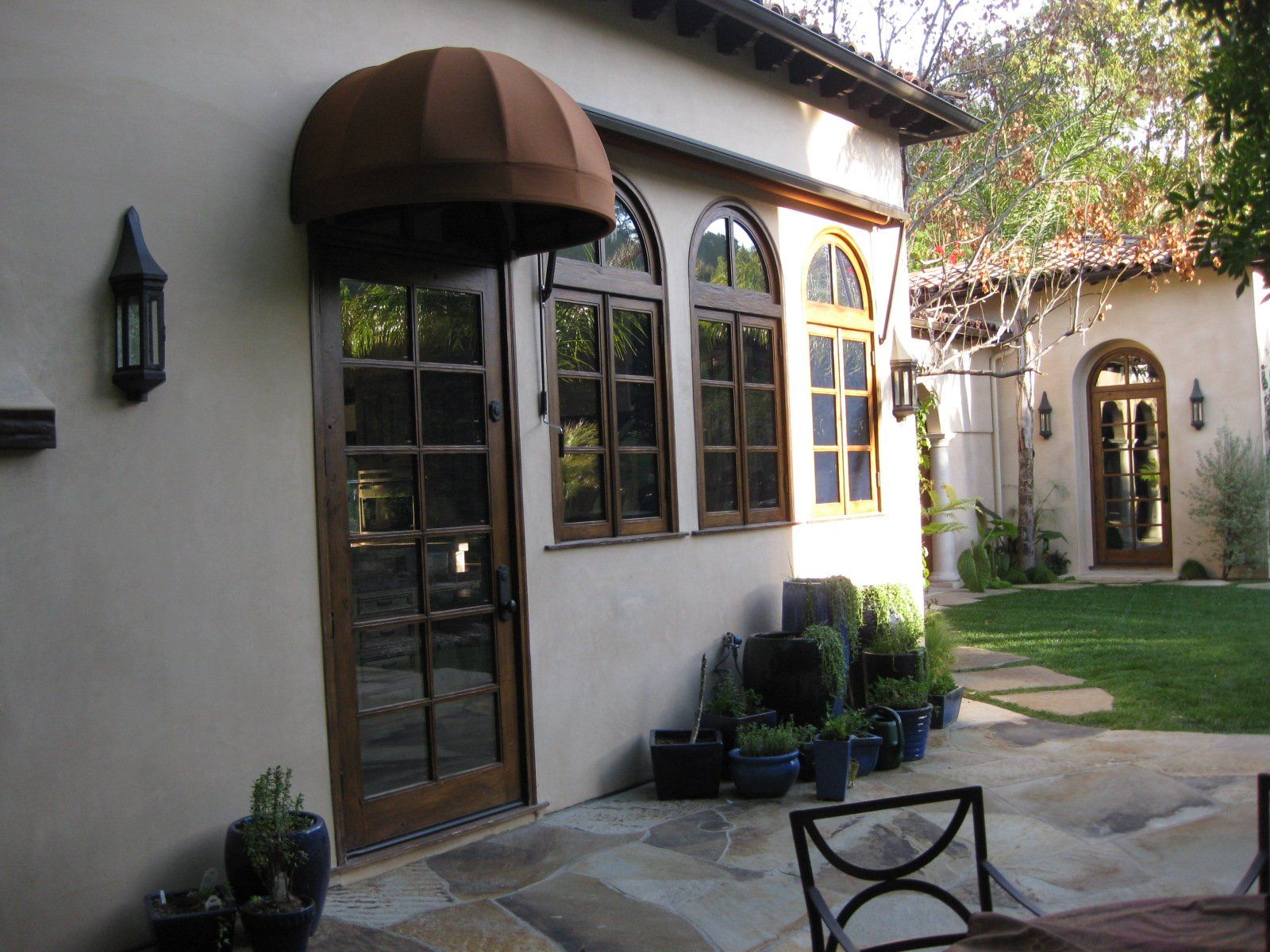 Courtyard patio with arched windows, brown awning, potted plants, and a stone walkway