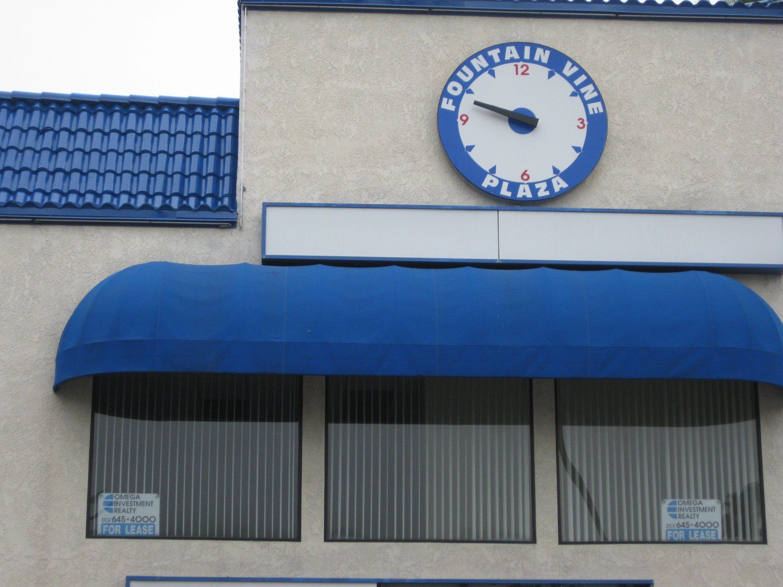 Facade of a building with a blue awning and a round wall clock above the entrance
