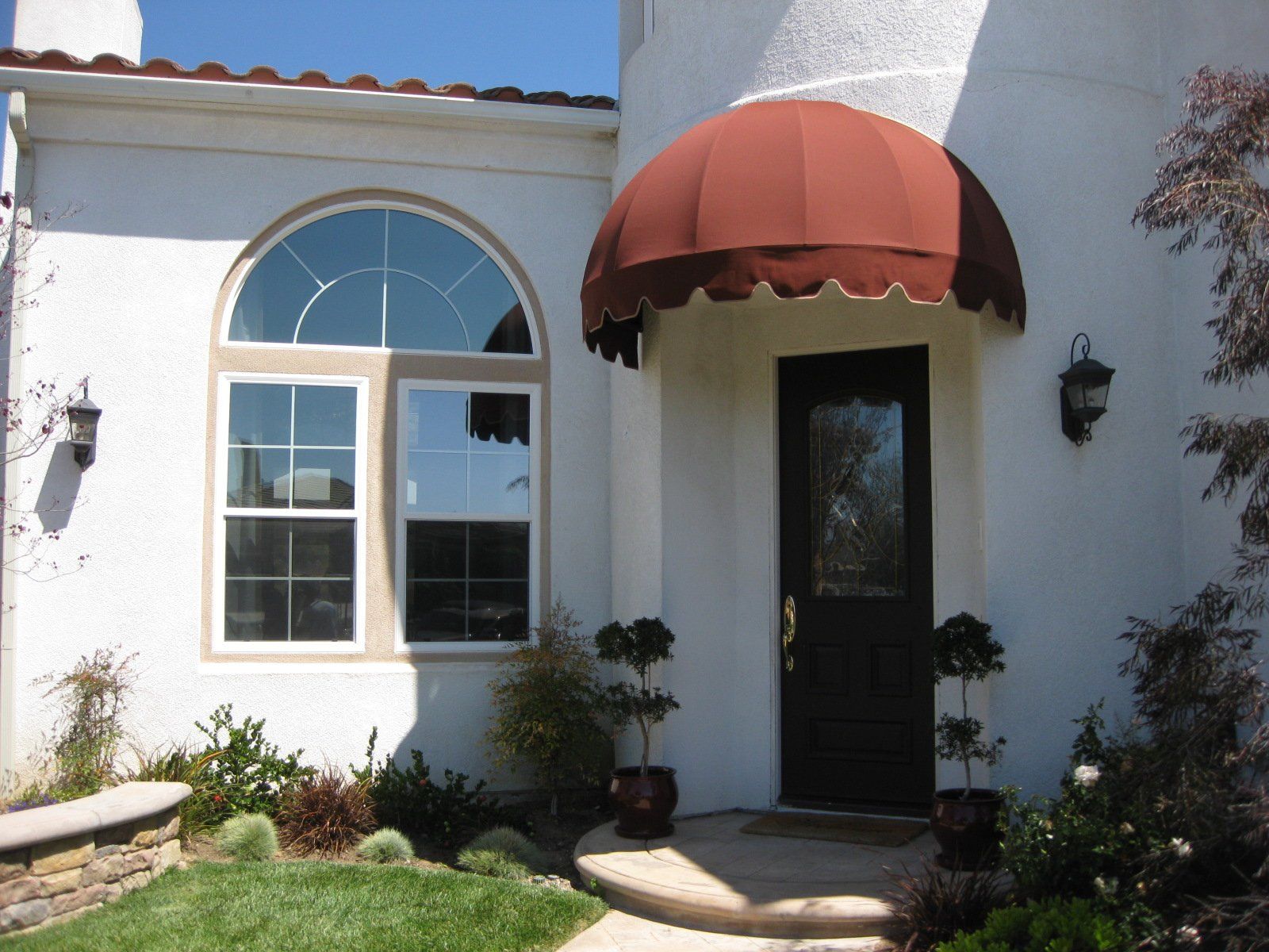 White stucco house entry with arched window and a red awning over a dark front door