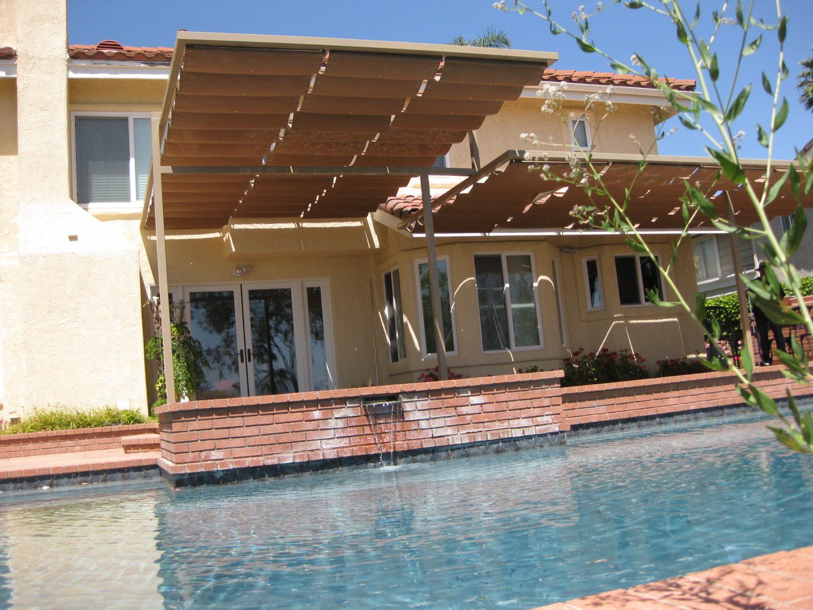 Backyard pool beside a house with a covered patio and brick trim